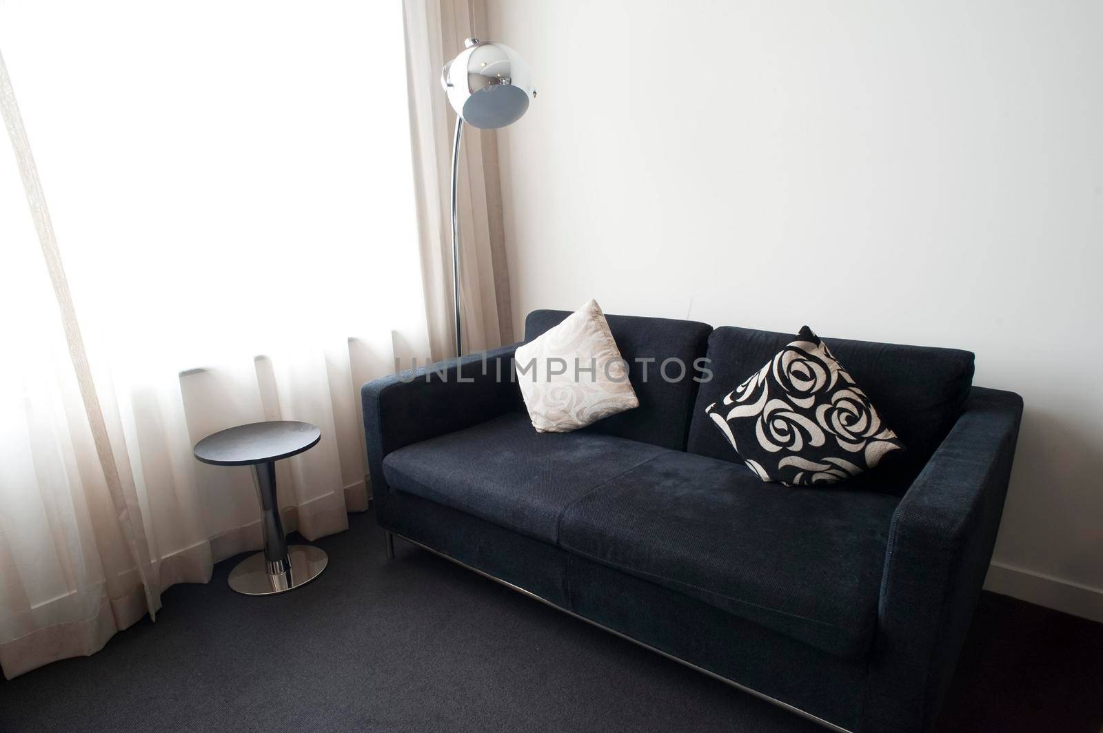 Modern living room decor in stylish black and white with a comfortable sofa, side tables and standard lamp alongside a floor height window