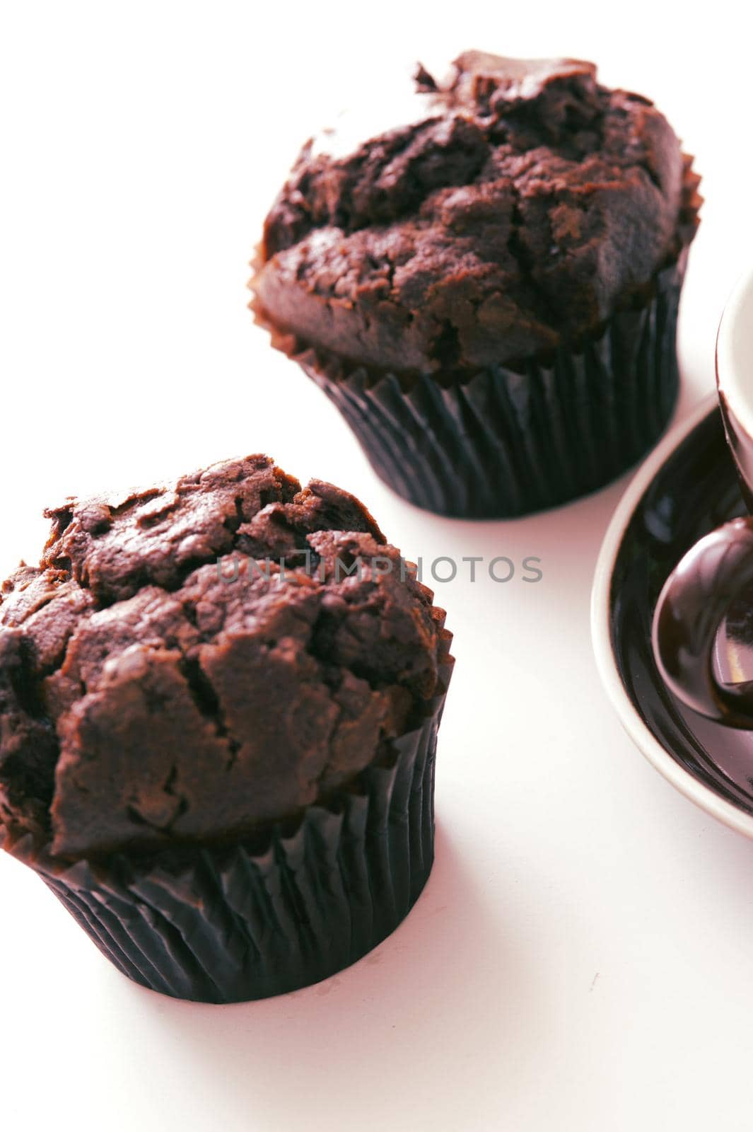 Tilted angle view on two freshly baked chocolate muffins on white table with subtle set down shadow