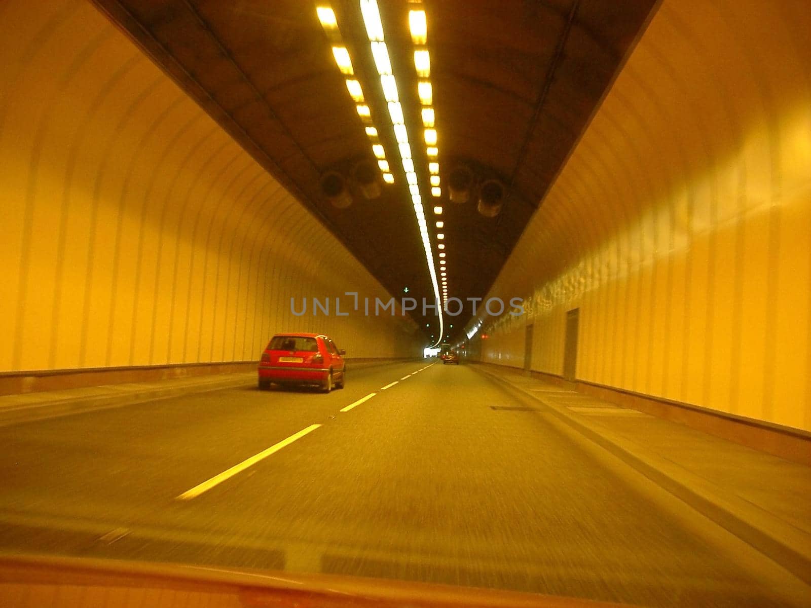 Car driving through a covered illuminated traffic tunnel causing air pollution through exhaust emission in the confined space