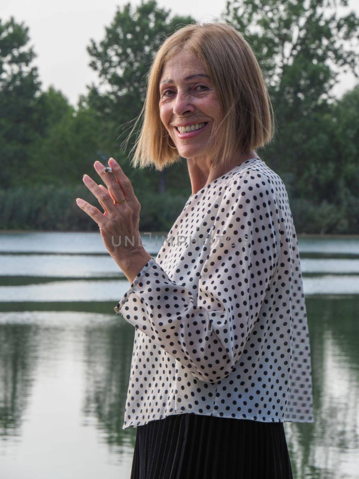 joyful senior woman smoking a cigarette in a park near the water by verbano