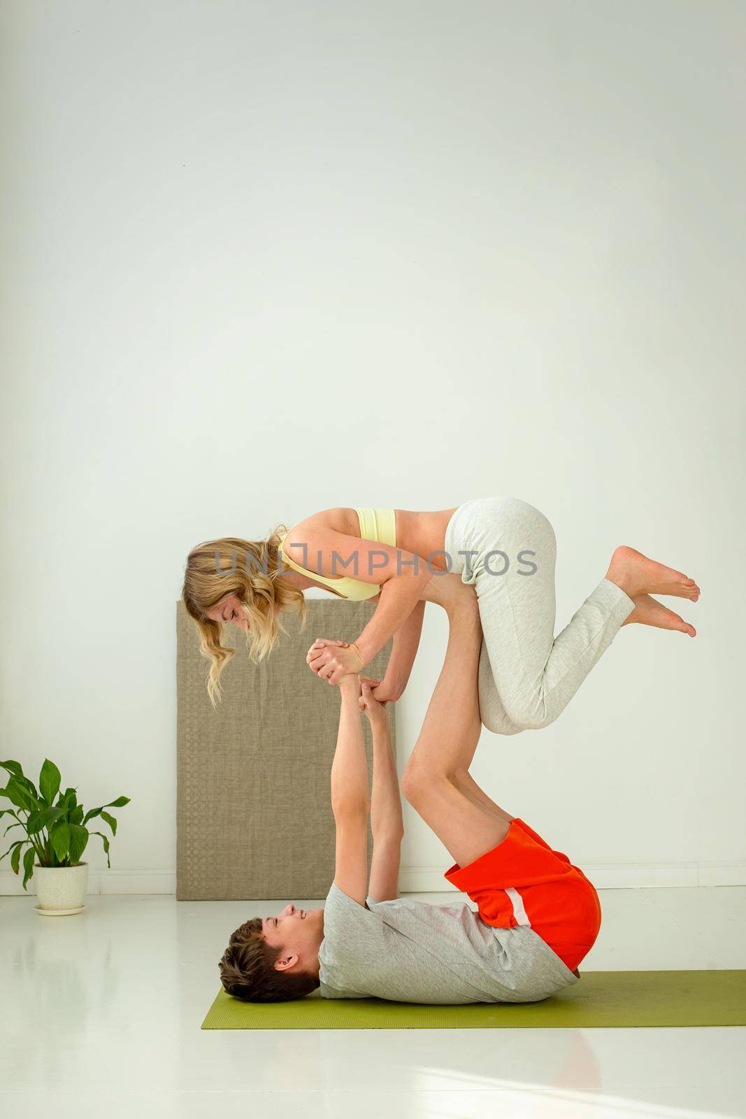 A guy in sportswear performs a yoga exercise while on a sports mat, paired with a slender woman. by Zakharova