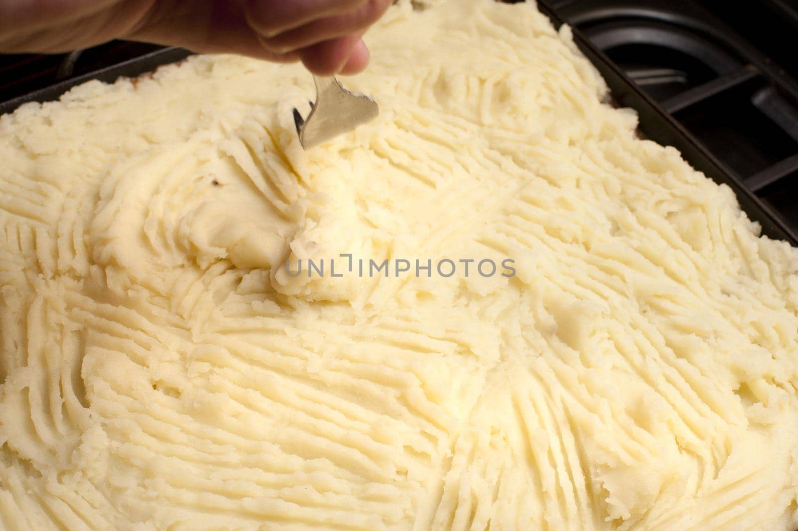 Cottage pie preparation with a cook smoothing the mashed potato crust over the meat with a fork before baking or grilling