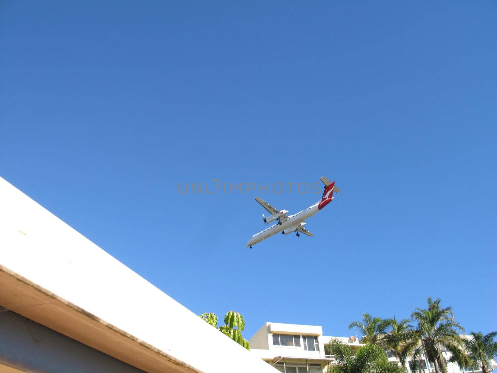 Aircraft coming on to land over the tops of whitewashed houses in a tropical resort conceptual of travel and summer vacations