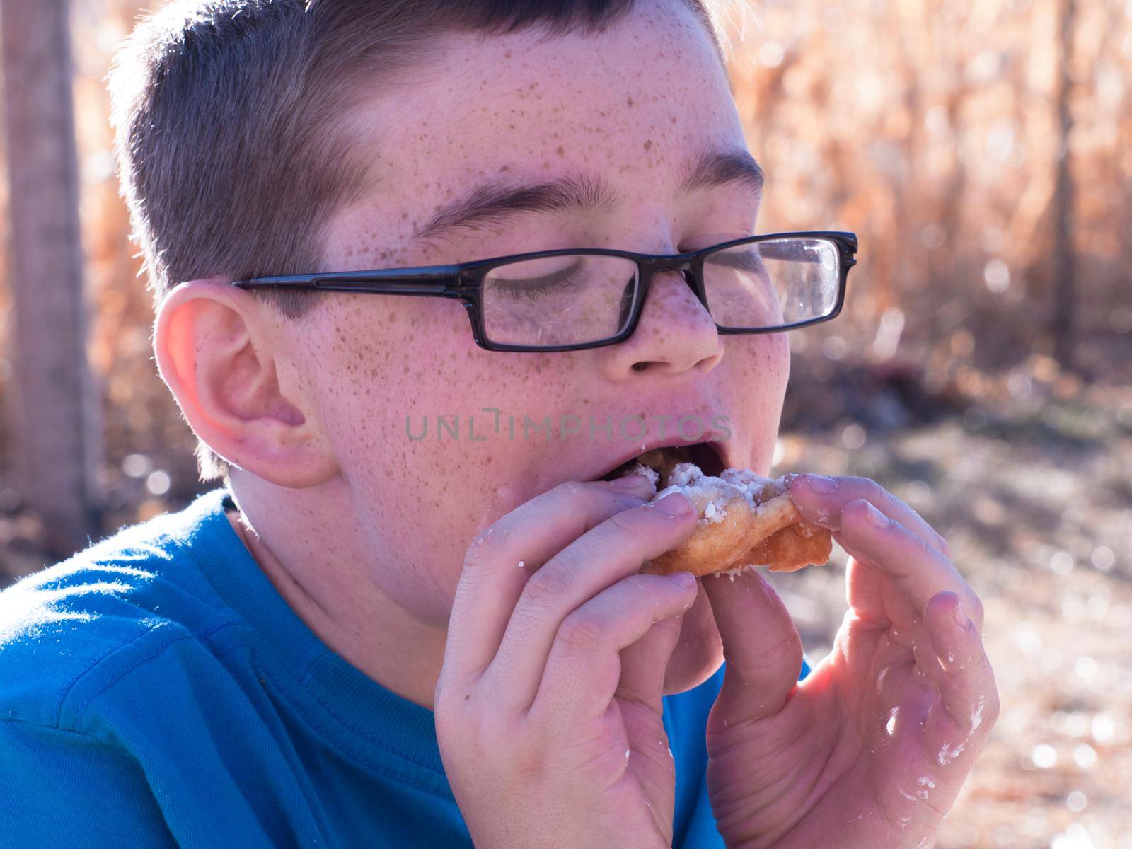 Young boy eating funnel cake in corn field.