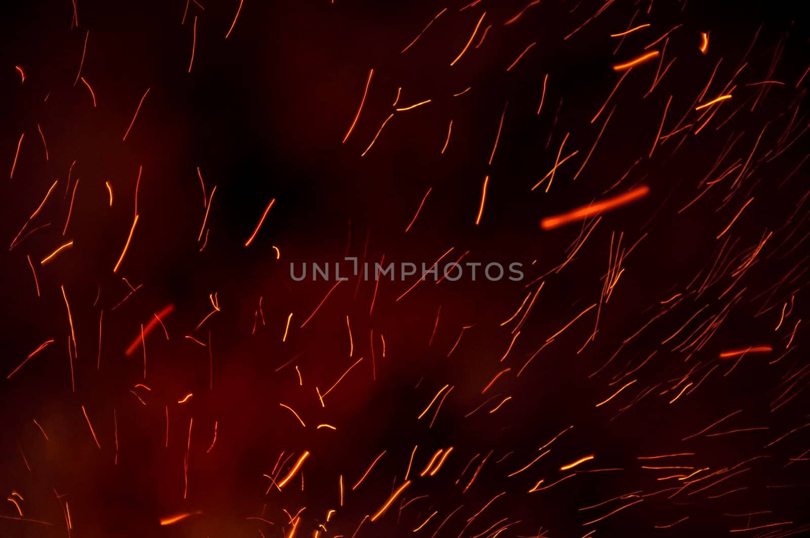 Background of fiery trails from glowing embers shooting through the darkness from a burning bonfire