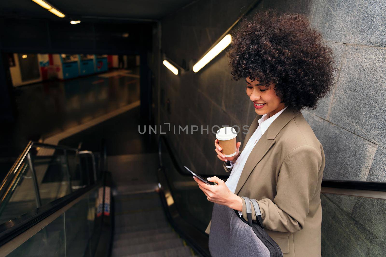 happy business woman checking phone on the escalator of the subway station, concept of urban lifestyle and public transport, copy space for text