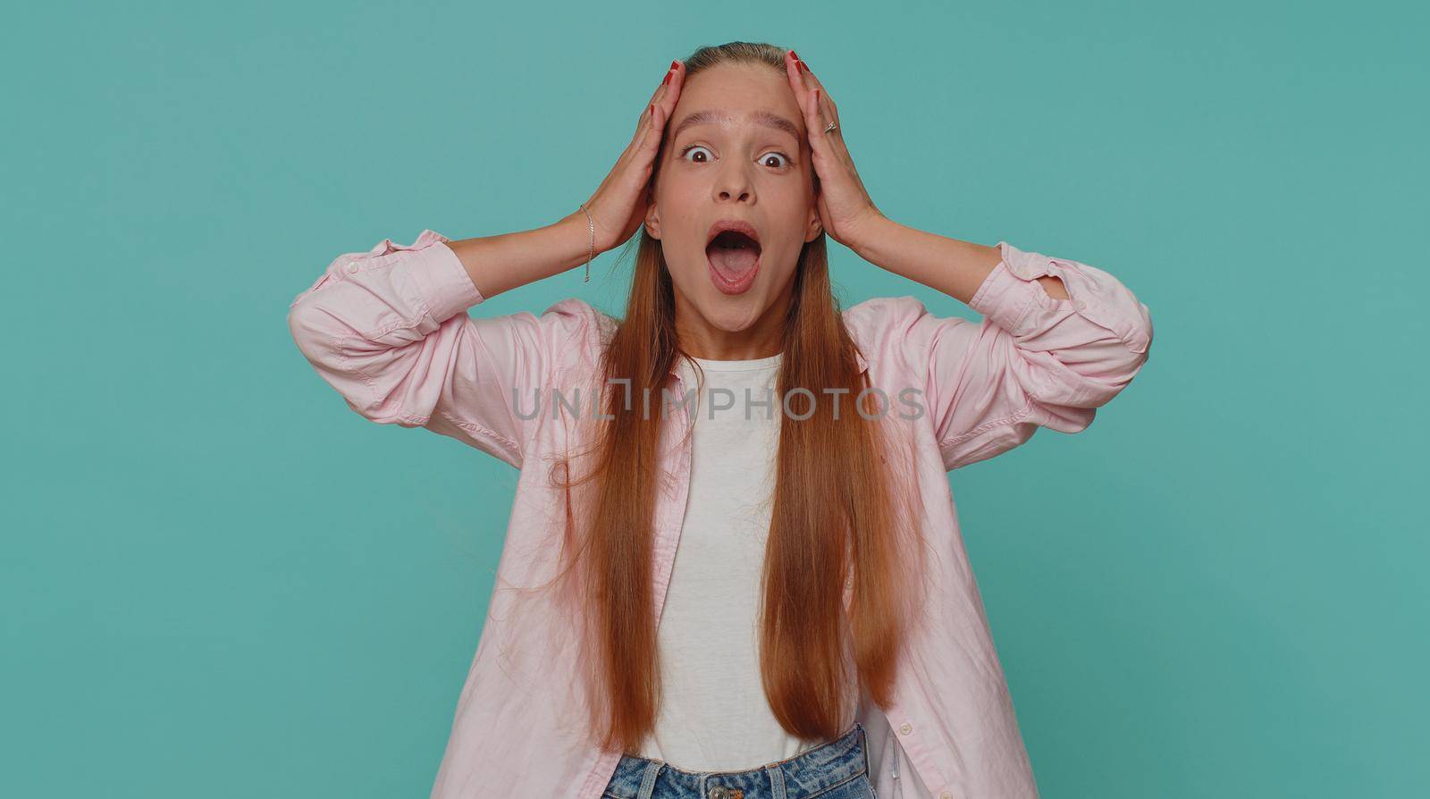 Oh my God, Wow. Excited amazed girl looking surprised at camera with big eyes, shocked by sudden victory game winning, lottery goal achievemen, good news. Child kid on blue studio background indoor