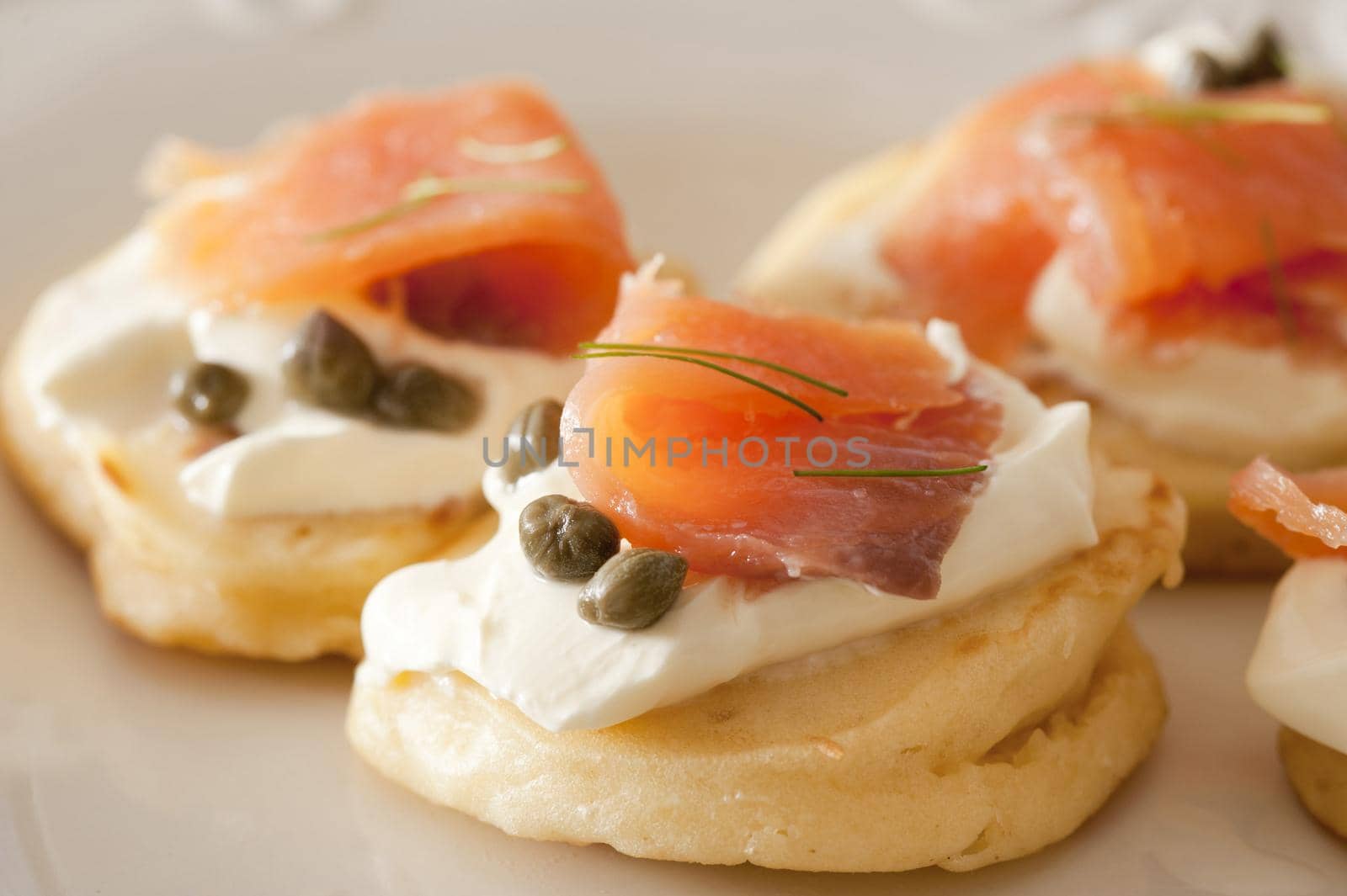 Close up view on delicious capers and raw fish blini appetizers showing smooth texture and little herb topping