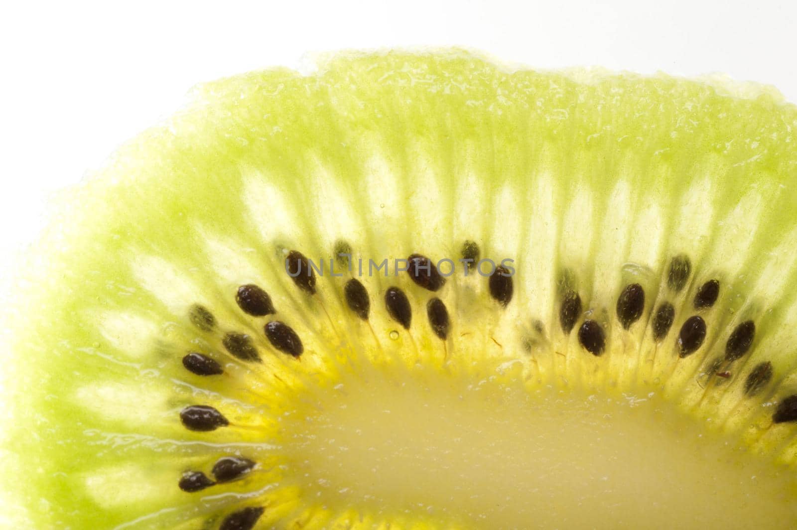 Macro detail of a slice peeled kiwifruit showing the interesting natural pattern of the juicy green flesh and pips on a white background