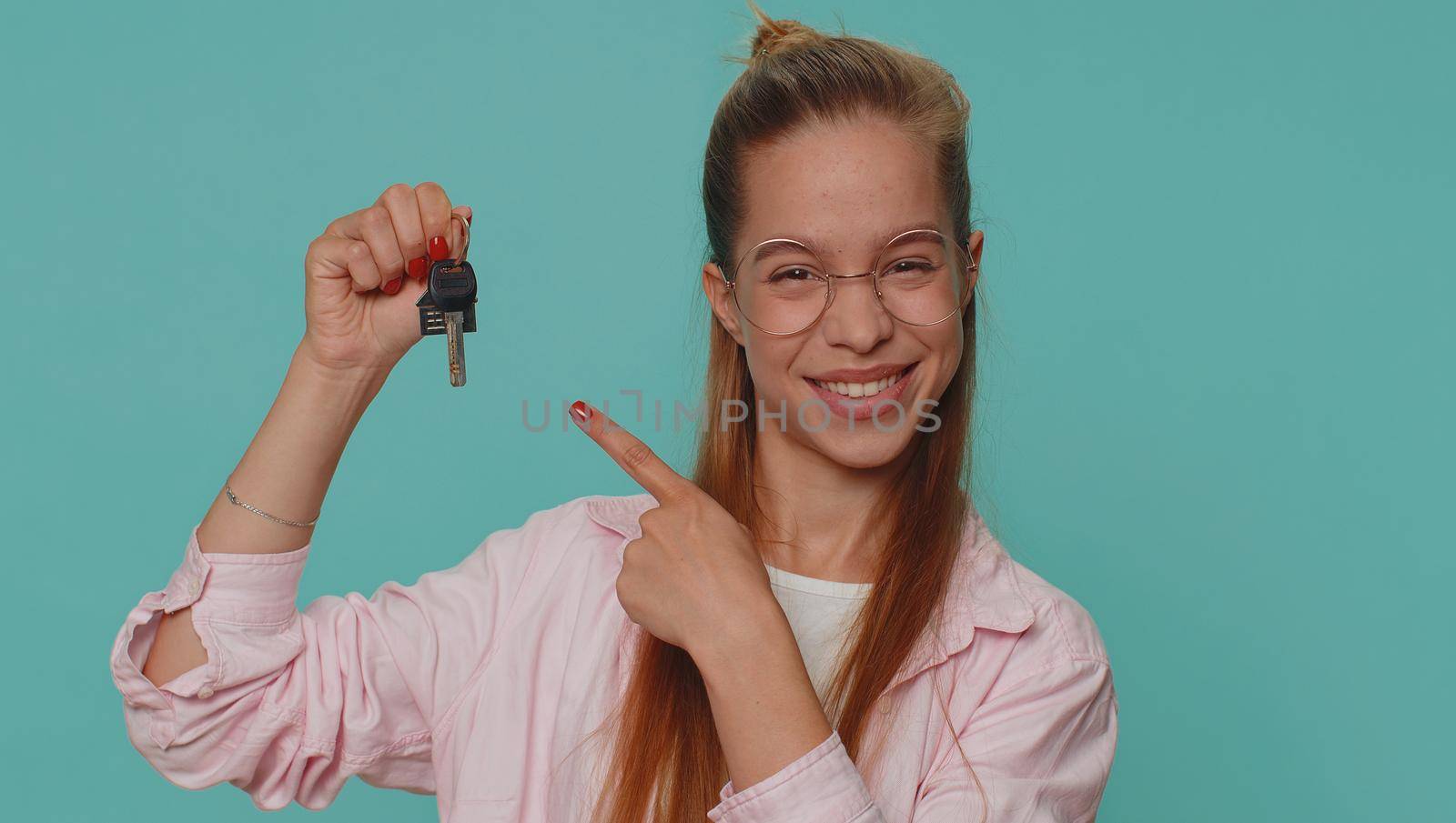 Teenager young girl real estate agent lifting hand showing the keys of new home house apartment, buying or renting property, mortgage loan. Student child kid isolated on blue studio background indoors