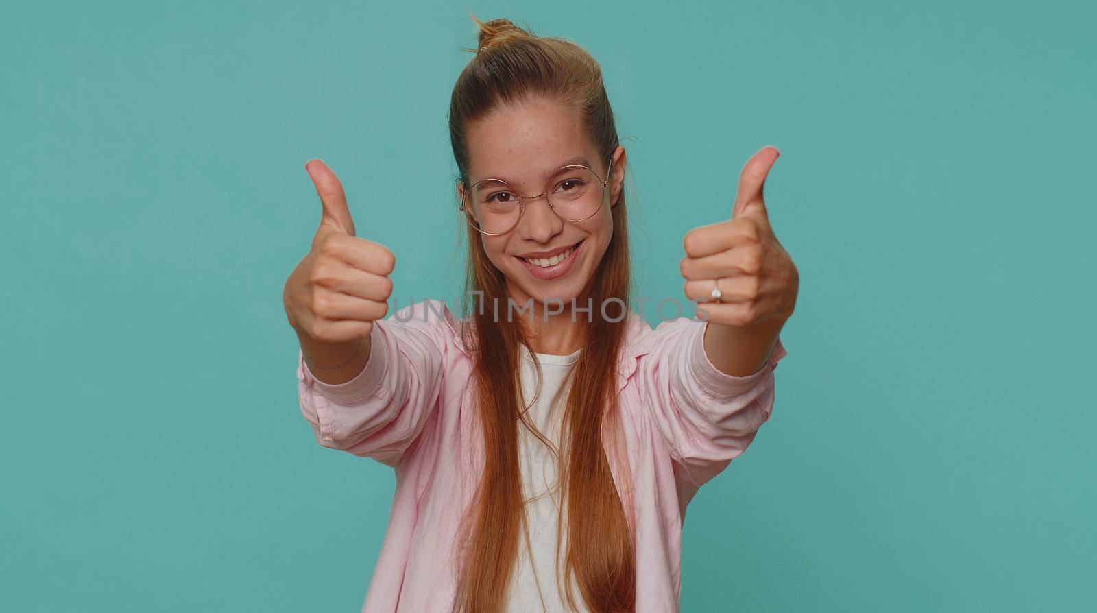 Like. Lovely pretty teenager girl raises thumbs up agrees with something or gives positive reply recommends advertisement likes good. Young stylish child kid isolated alone on blue studio background