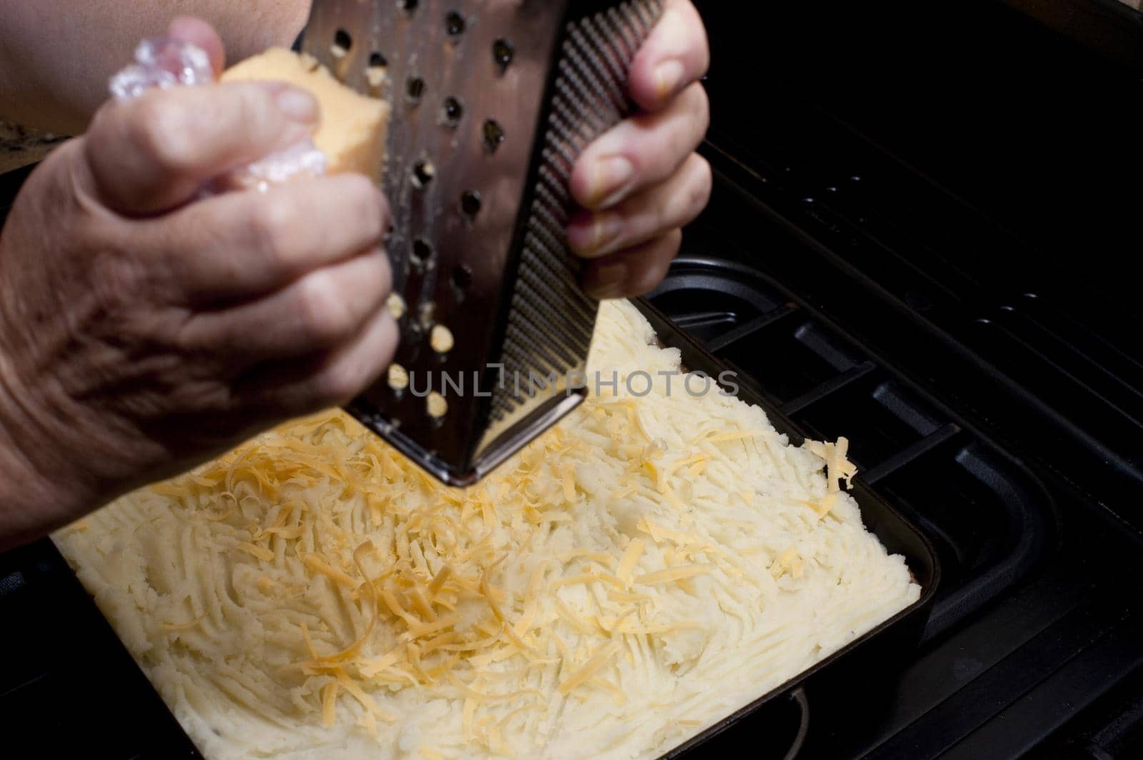 Grating cheese over the mashed potato topping on a cottage pie before place it in the oven to bake or grill