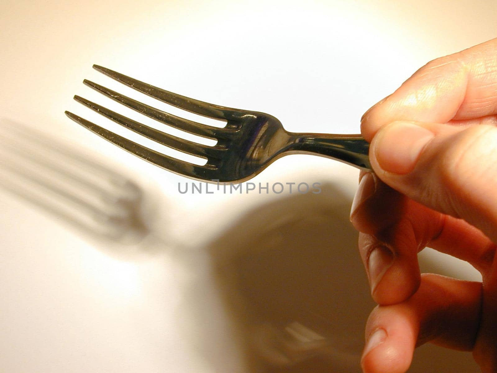 Close up of the fingers of a man holding a fork casting a shadow onto a white plate