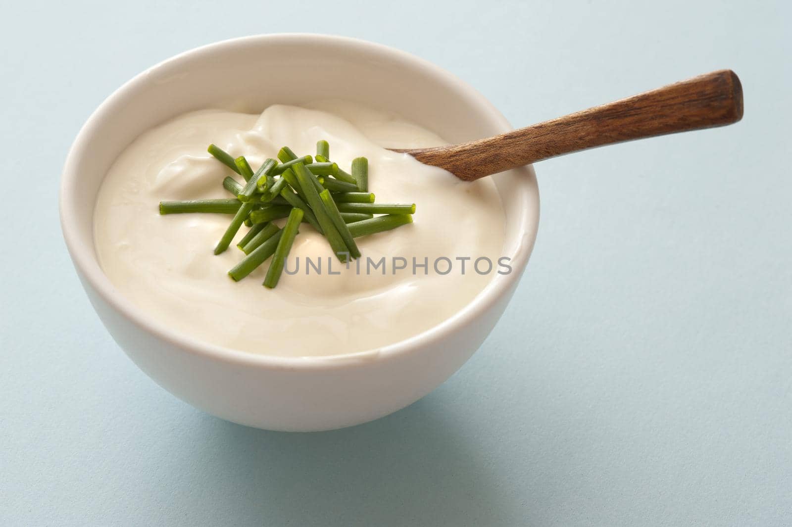 Side dish of sour cream and fresh chopped green chives with a small wooden spoon to accompany a meal as a topping or garnish