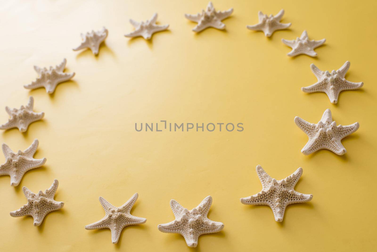 Circle of clean white dried starfish on a yellow background with copy space for your marine, nautical or summer vacation themes
