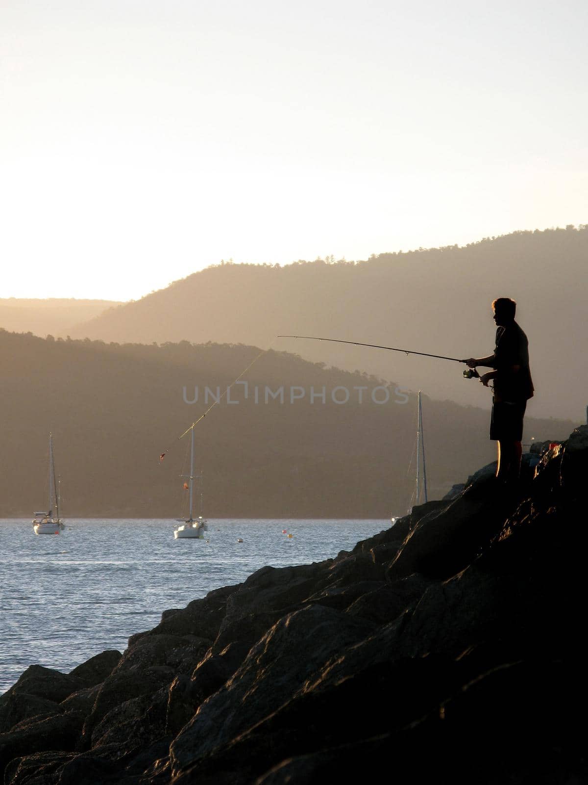 a man fishing at sunset from a marina wall