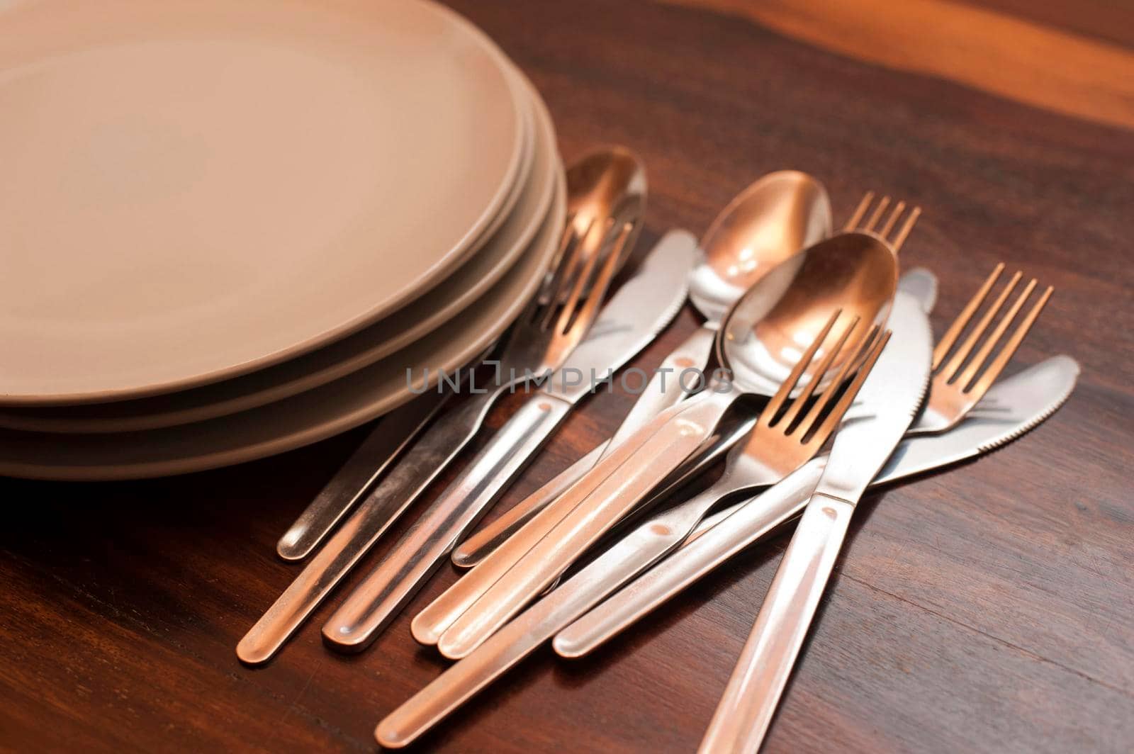 Loose cutlery and a stack of empty plates on a buffet table with knives, forks and spoons on a wooden tabletop