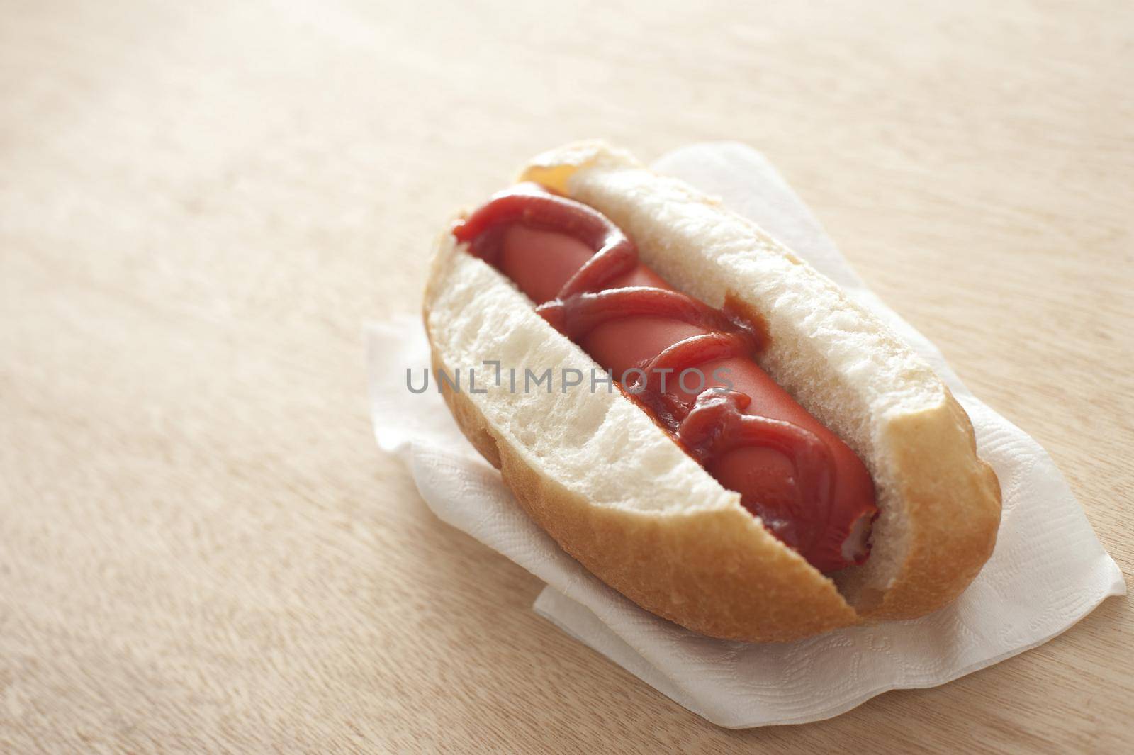 Hot dog and ketchup on a fresh white bread roll with a grilled smoked Wiener sausage served as a fast food snack on a paper serviette, with copy space