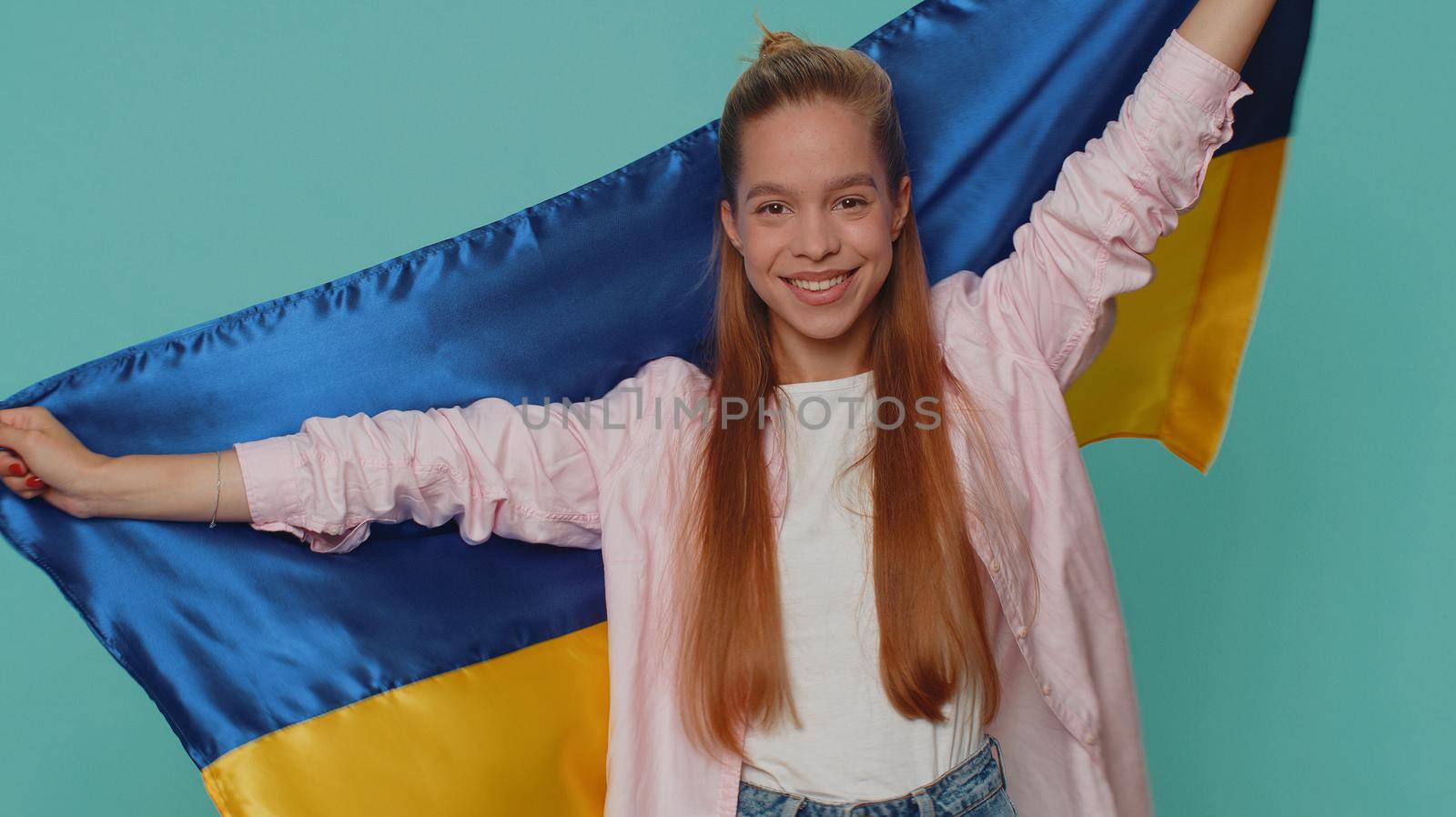 Teen young girl hold Ukraine national flag hoping for success, smiling with kind optimistic expression. Independence, freedom, victory in war, national holiday. Student child kid on blue background