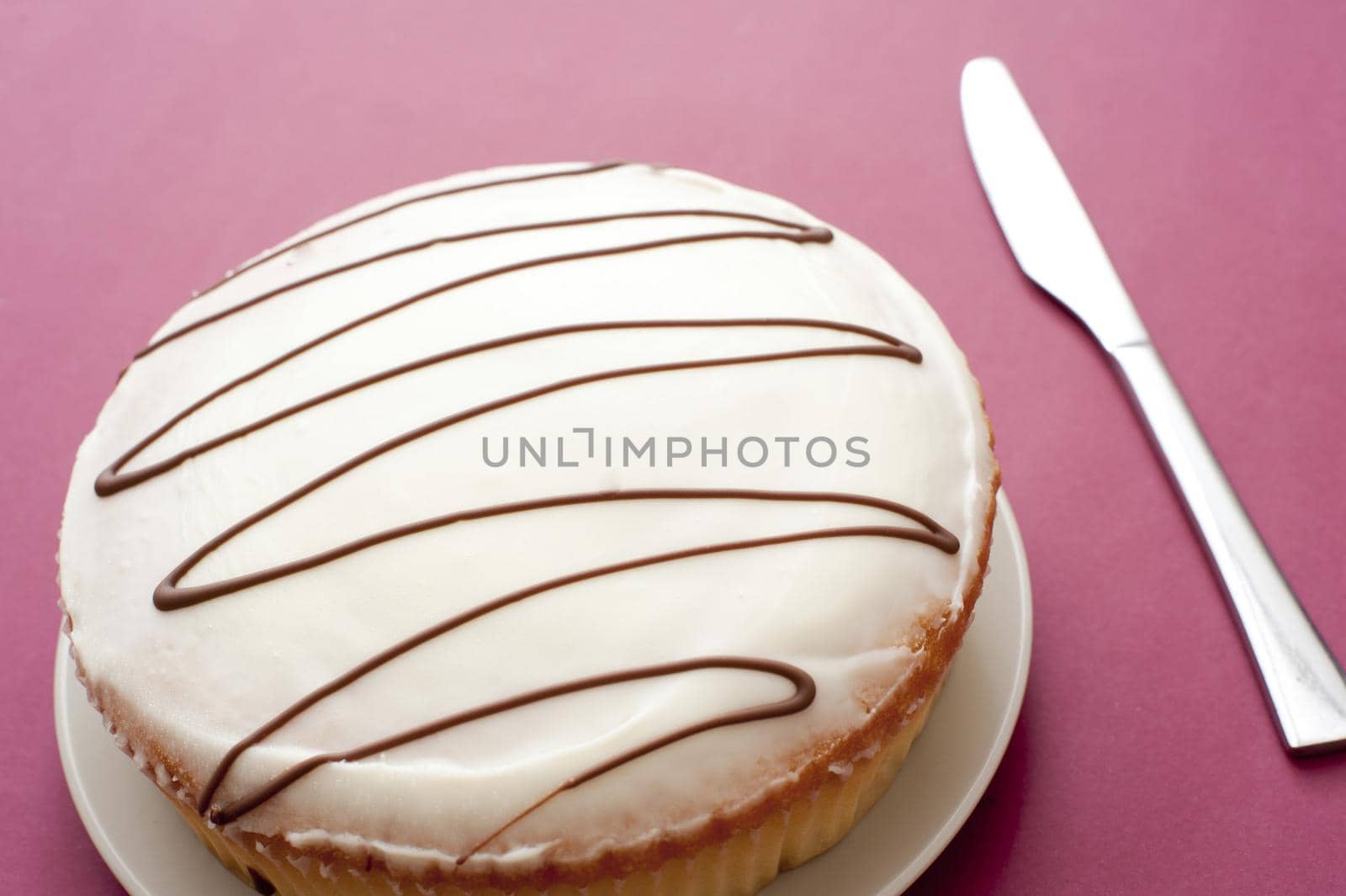 Plain iced cake with a zigzag pattern on the icing and knife alongside to cut it over a red background