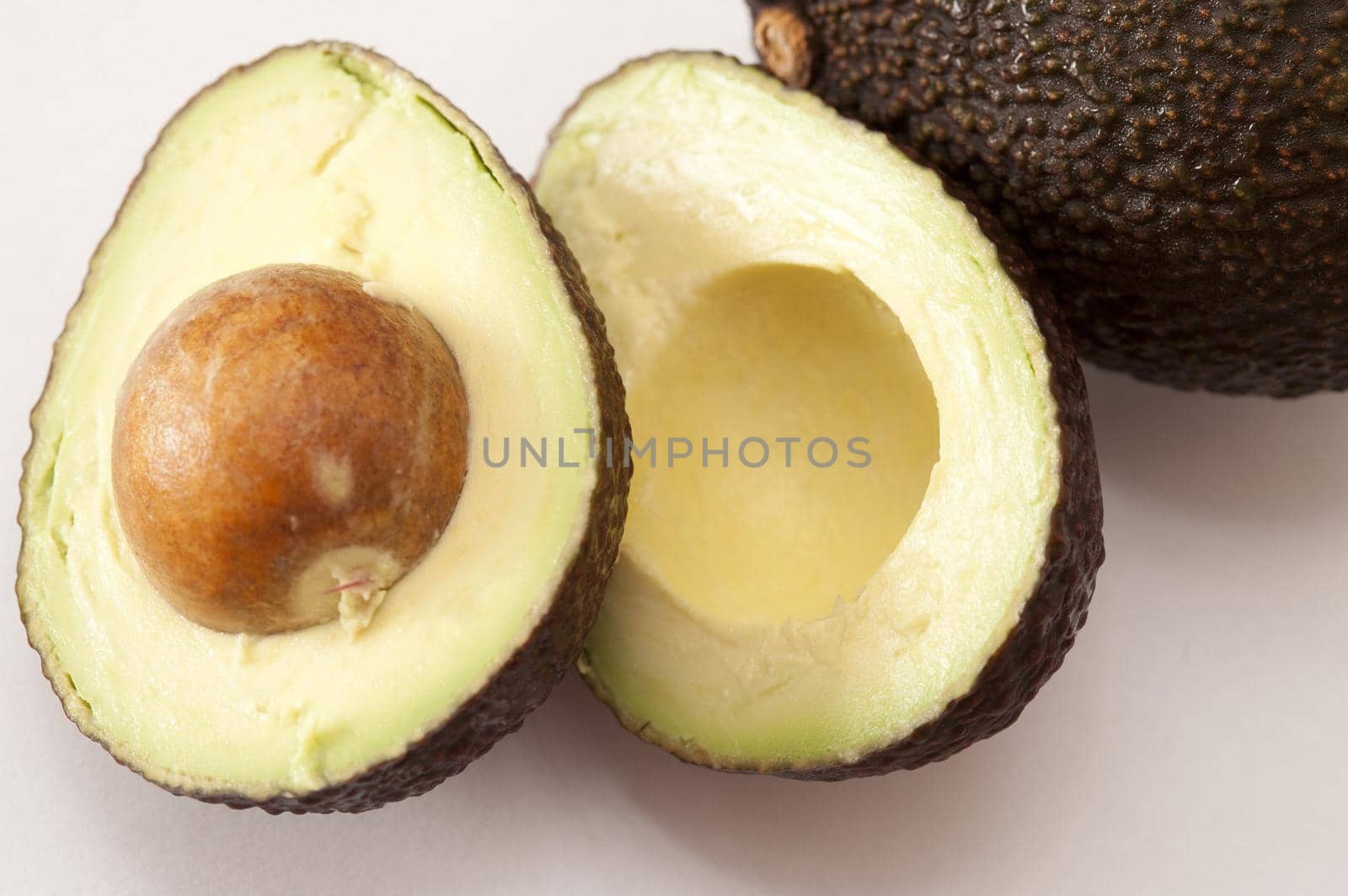 Halved fresh ripe avocado pear with the pip still intact in the one half showing the soft pulpy flesh with its exotic flavor making it a popular salad ingredient