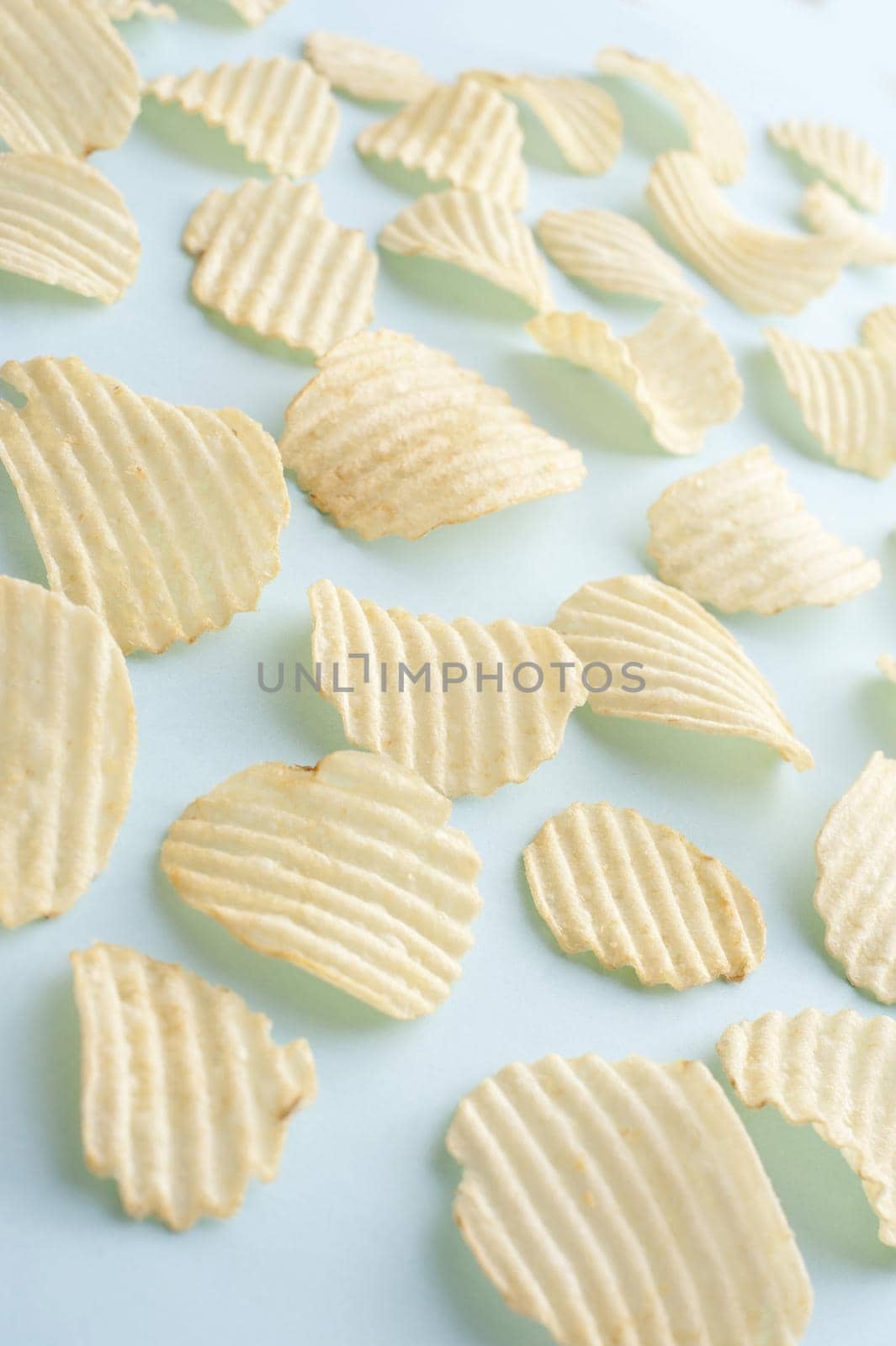 Background of scattered crinkle cut potato crisps on a light green background viewed high angle for a tasty but unhealthy snack