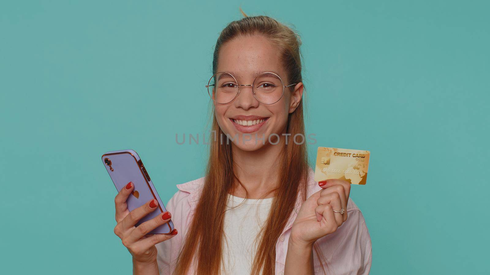 Happy teenager girl use smartphone, plastic credit bank card, browsing say wow yes, found out great big win, success lotter, good news, purchases online shopping. Child kid on blue studio background