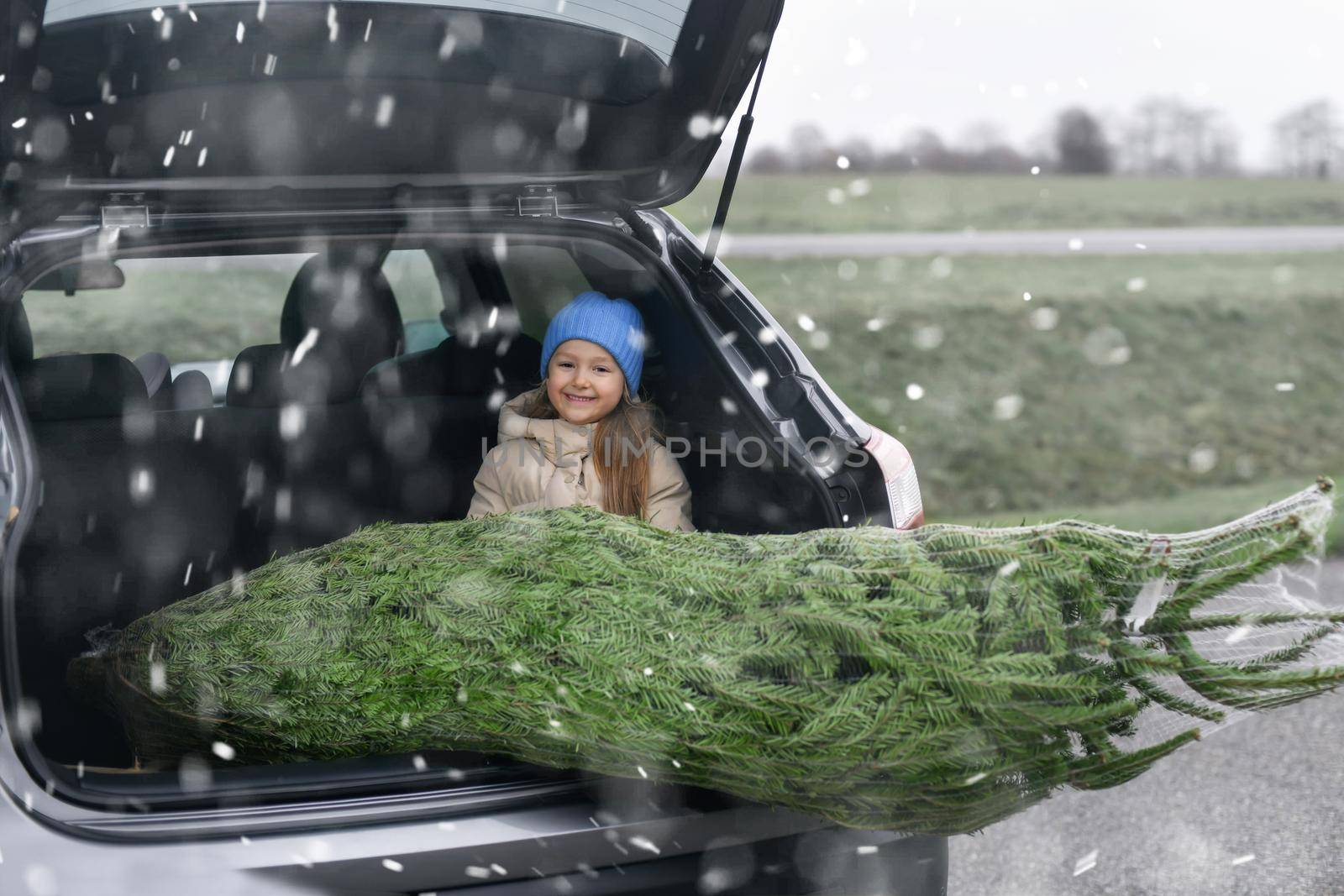 A girl sitting in the trunk with a Christmas tree