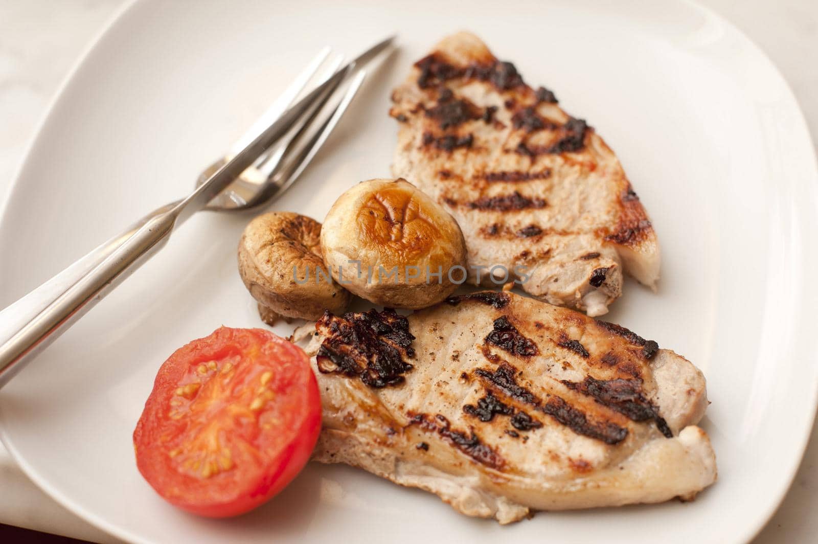 Two delicious lean healthy grilled pork chops served with tomato and mushrooms, high angle view