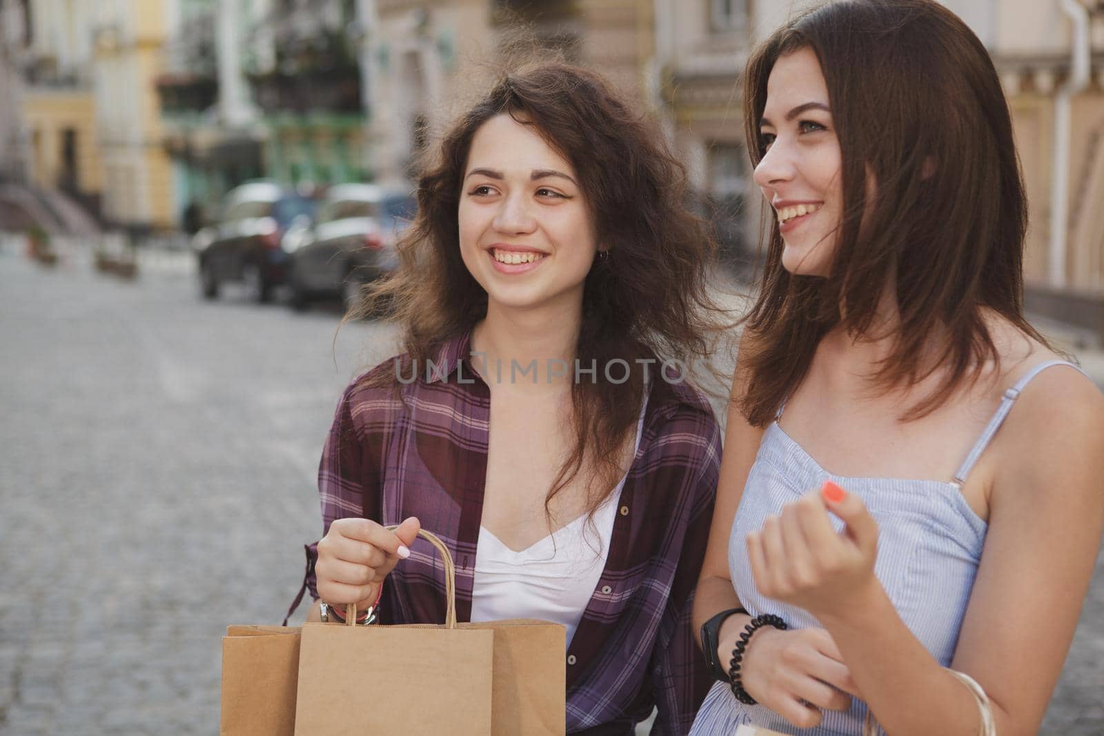 Happy young female friends laughing, walking city streets, carrying shopping bags. Vacation, sighseeing, traveling concept
