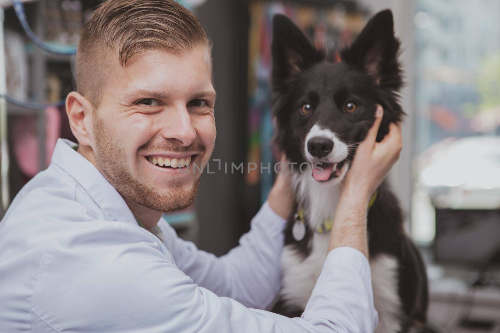 Handsome happy male veterinarian laughing to the camera, petting adorable dog at his clinic. Cute black puppy being examined by professional vet doctor. Happiness, animals, love concept