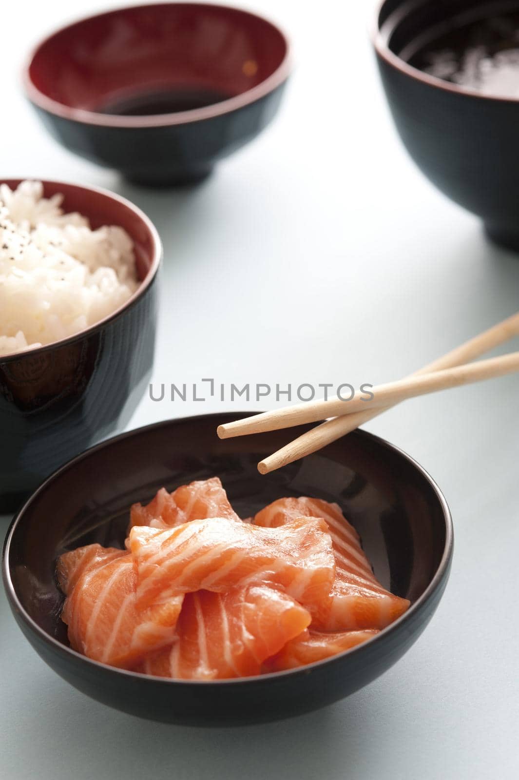 Fresh salmon dinner with chopsticks in black bowl besides serving of white rice and soy dipping sauce