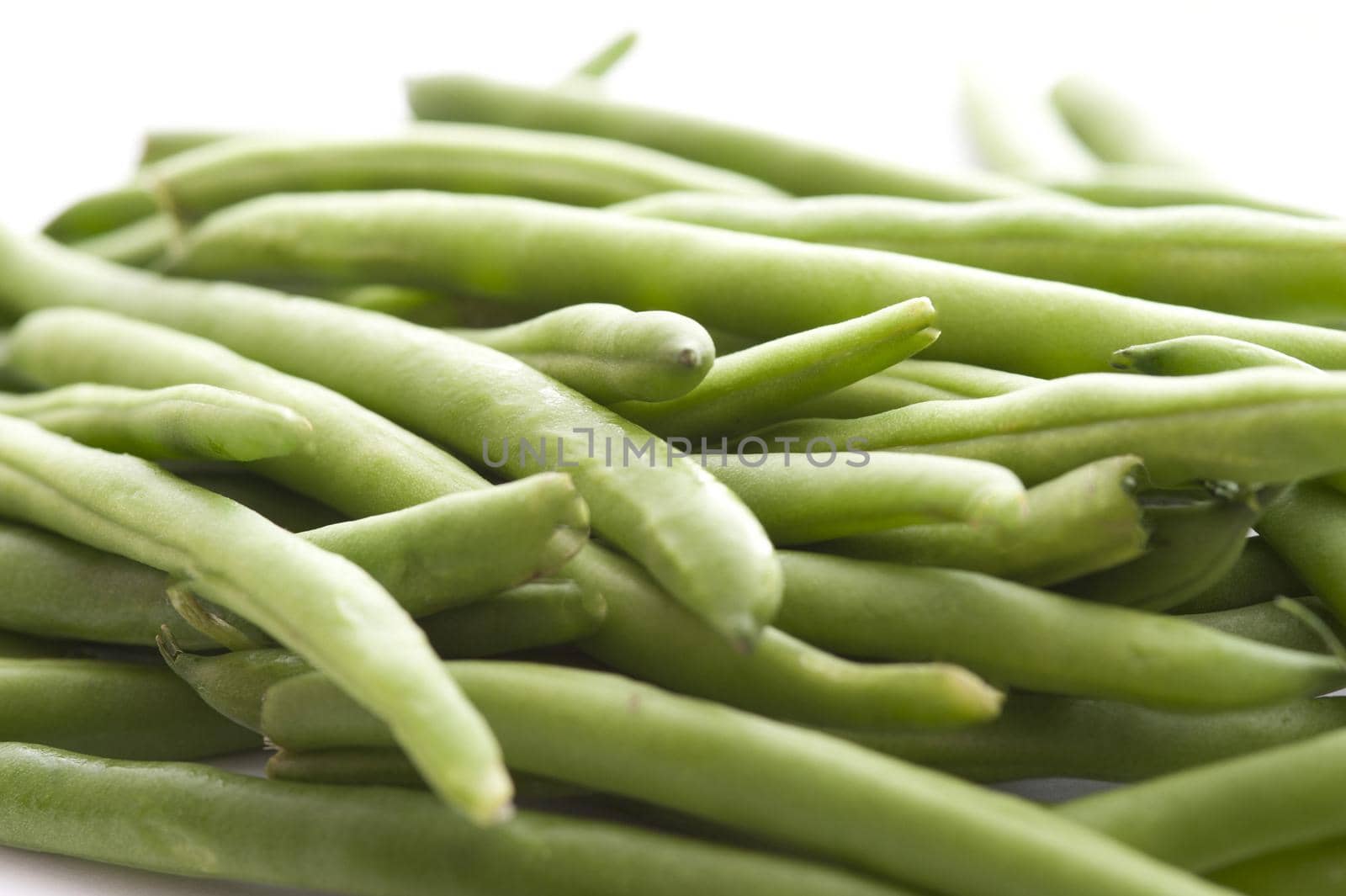 Heap of whole fresh green uncooked string or runner beans viewed low angle over white