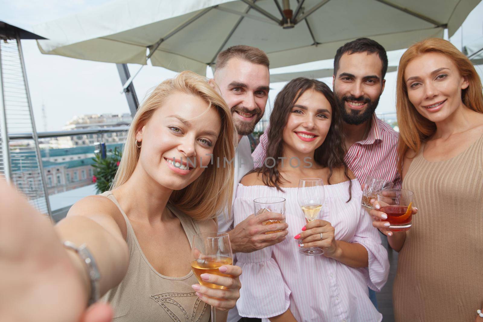 Beautiful woman taking selfie with her friends while drinking on rooftop party in the city
