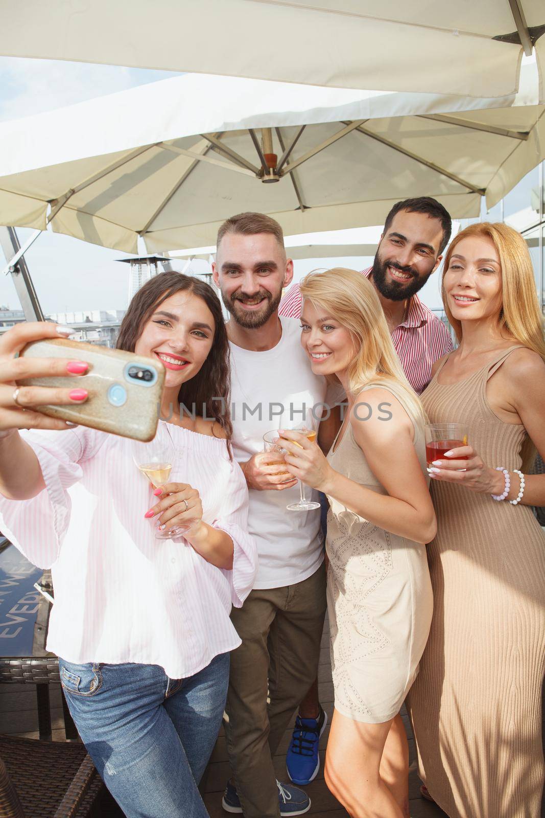 Vertical shot of a group of young people celebrating summer on rooftop party, taking selfies with smart phone