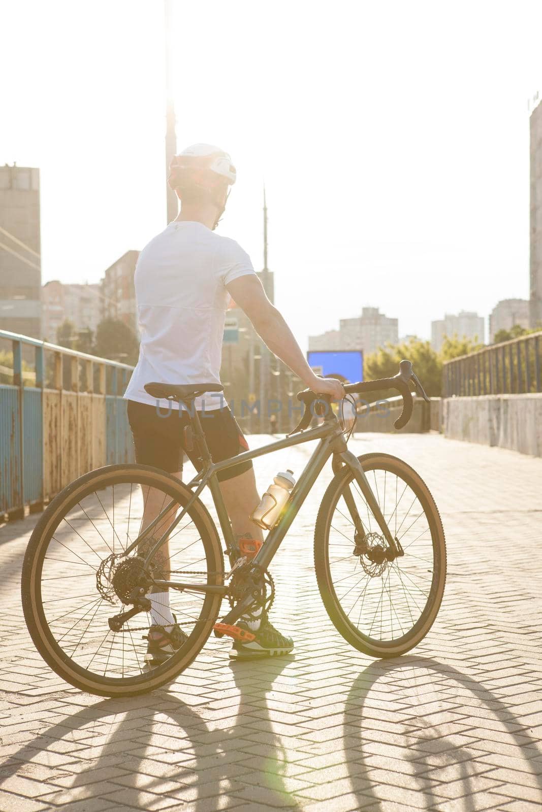 Vertical rear view shot of a male cyclist in helmet standing with his bike outdoors