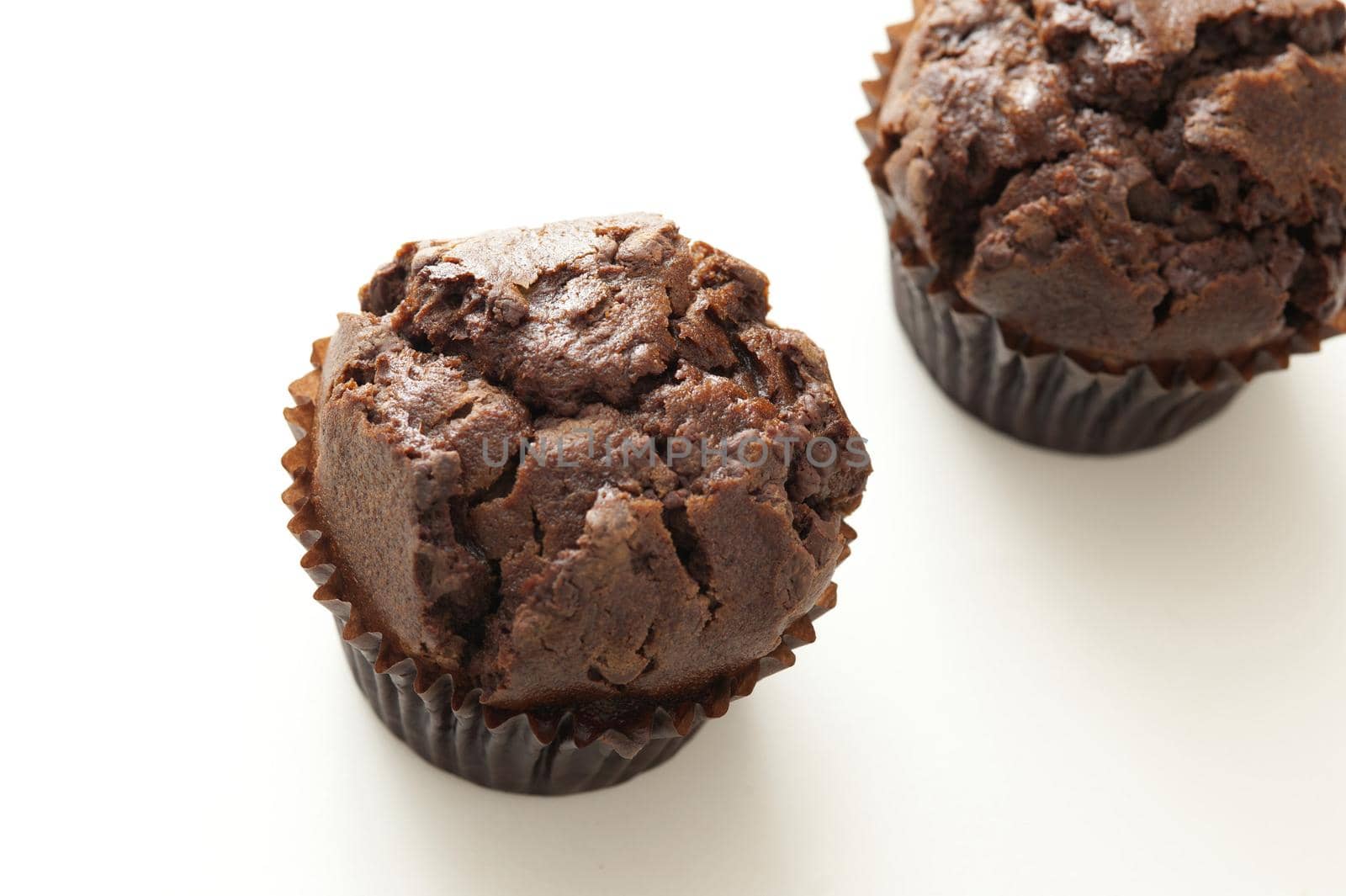 Two freshly baked dark chocolate muffins or cupcakes on a white background with copy space, high angle view
