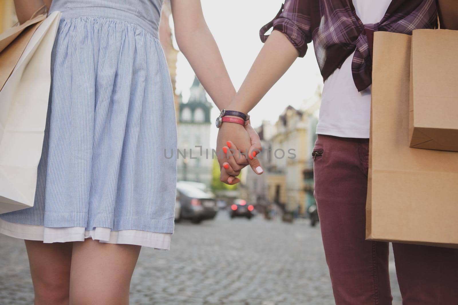 Cropped shot of two women holding hand, walking in the city with shopping bags. Female friends enjoying sightseeing on their vacation, holding hands