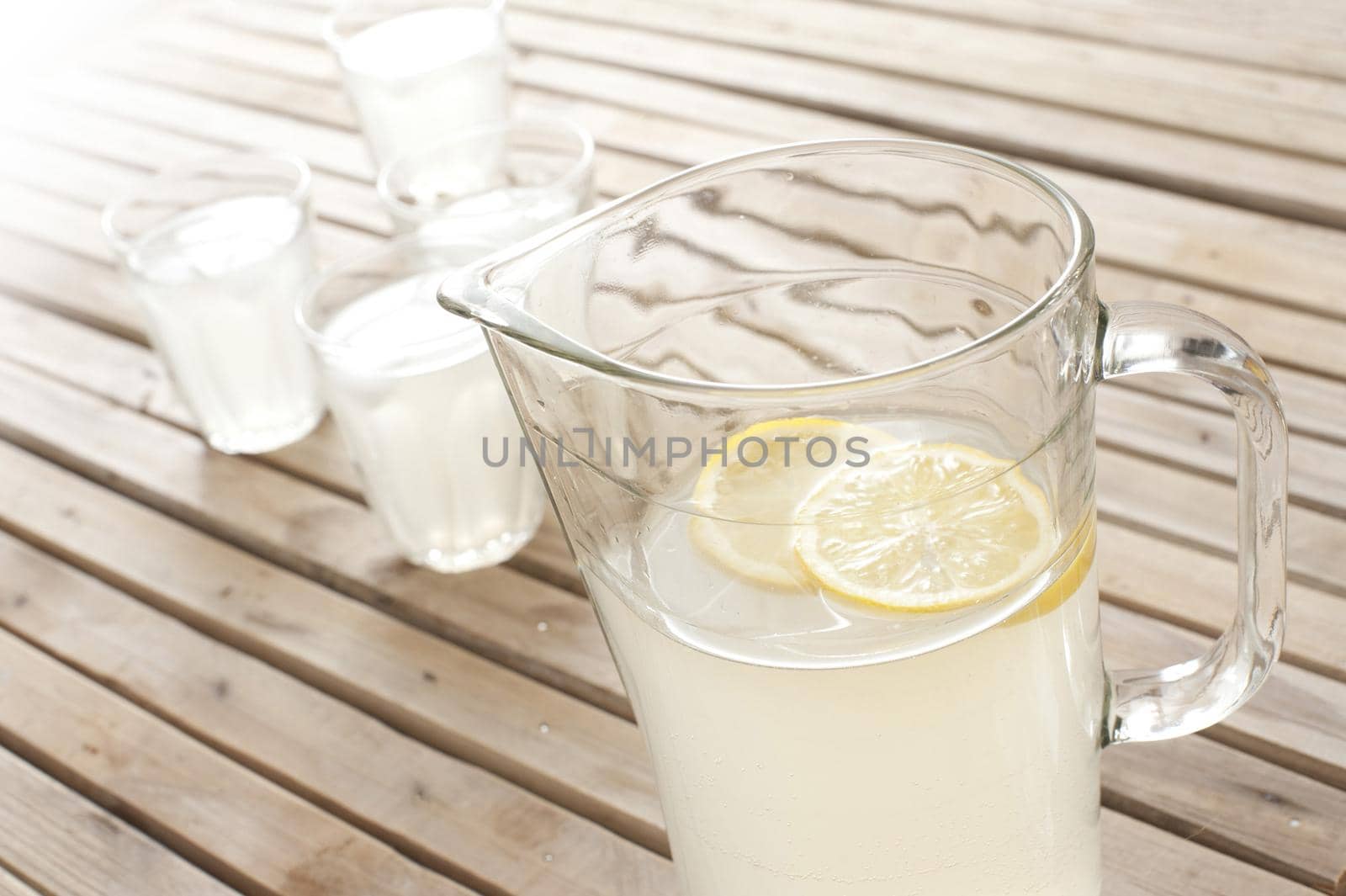 Fresh homemade lemonade in a jug with full glasses on an outdoor wooden picnic table for a refreshing summer beverage, high angle view