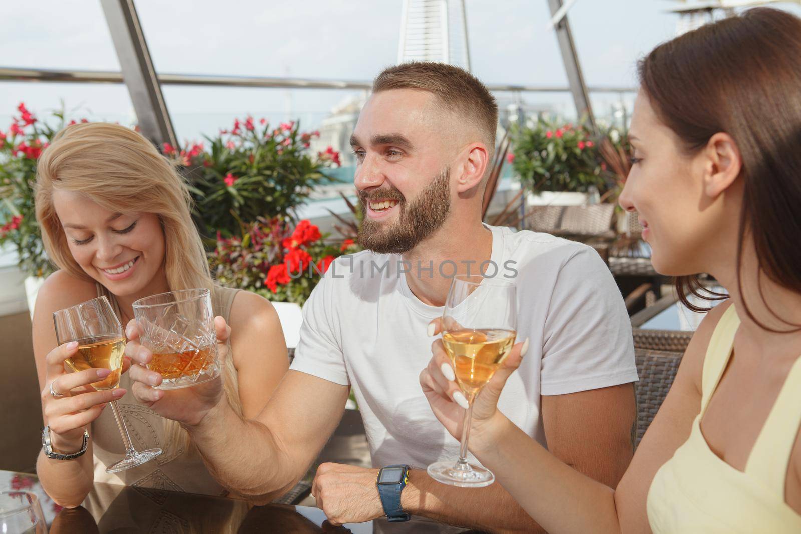 Group of friends laughing, drinking wine together at rooftop bar