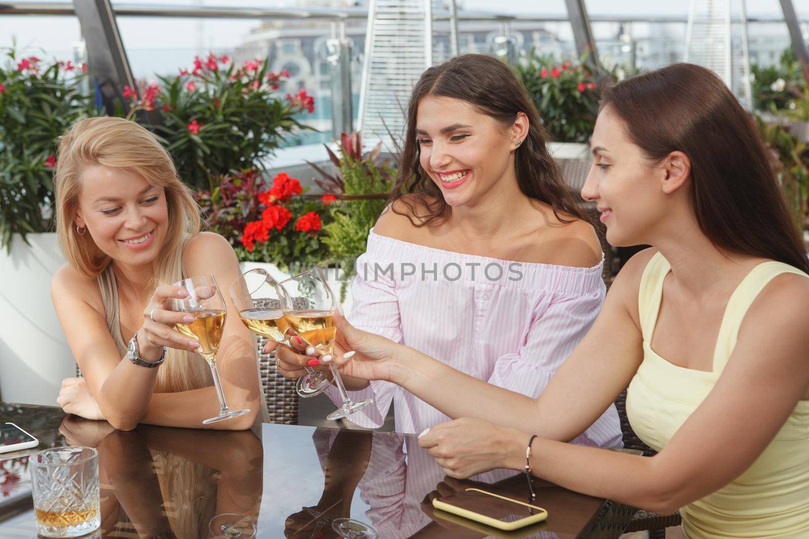 Beautiful young female friends celebrating together at rooftop bar, clinking wine glasses