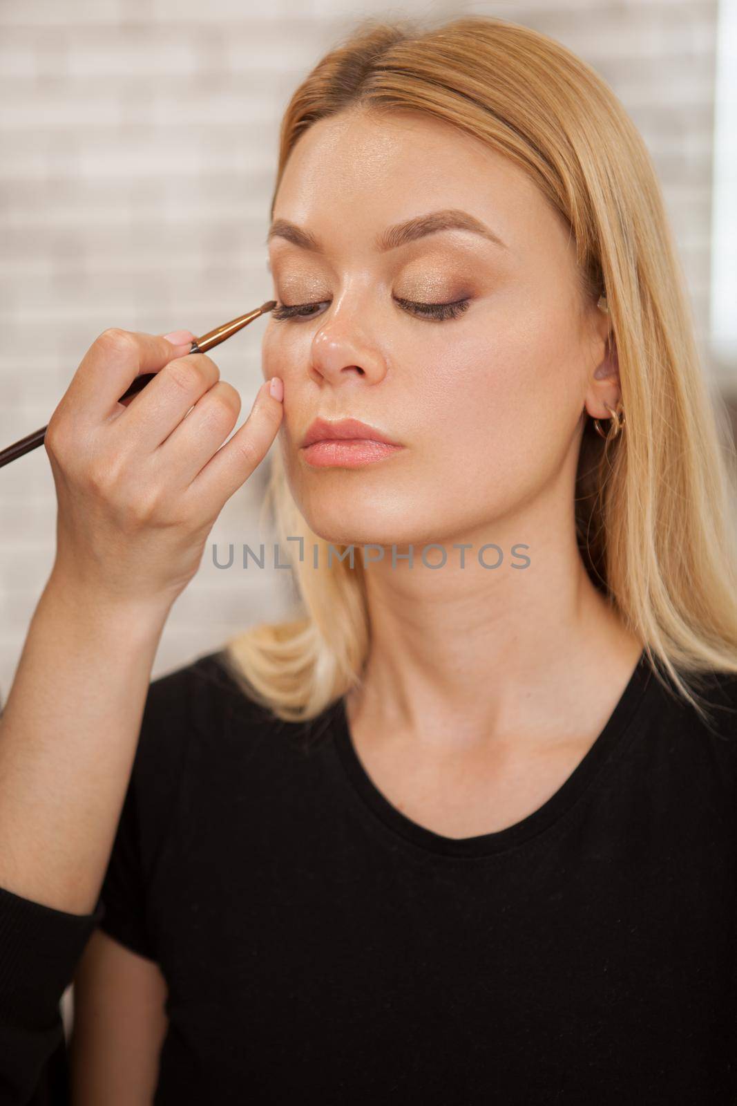 Vertical shot of a professional makeup artist working at beauty studio, preparing female model for photoshoot