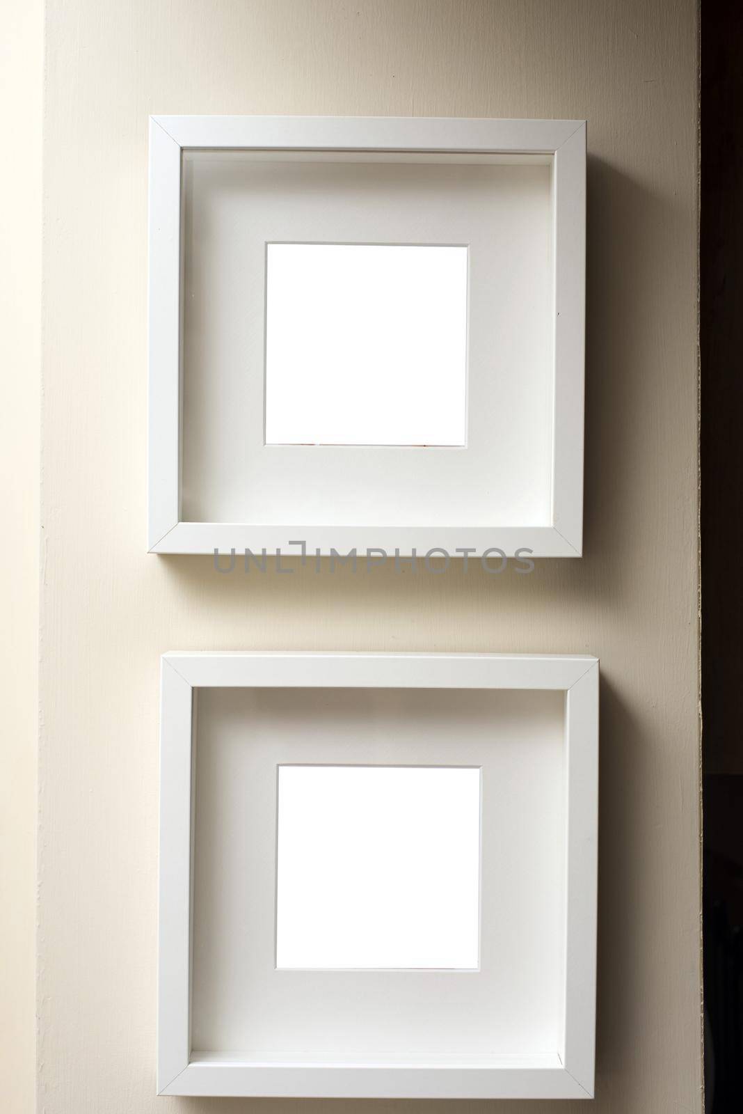 Two empty square neutral colored frames hanging together on an off white wall one below the other