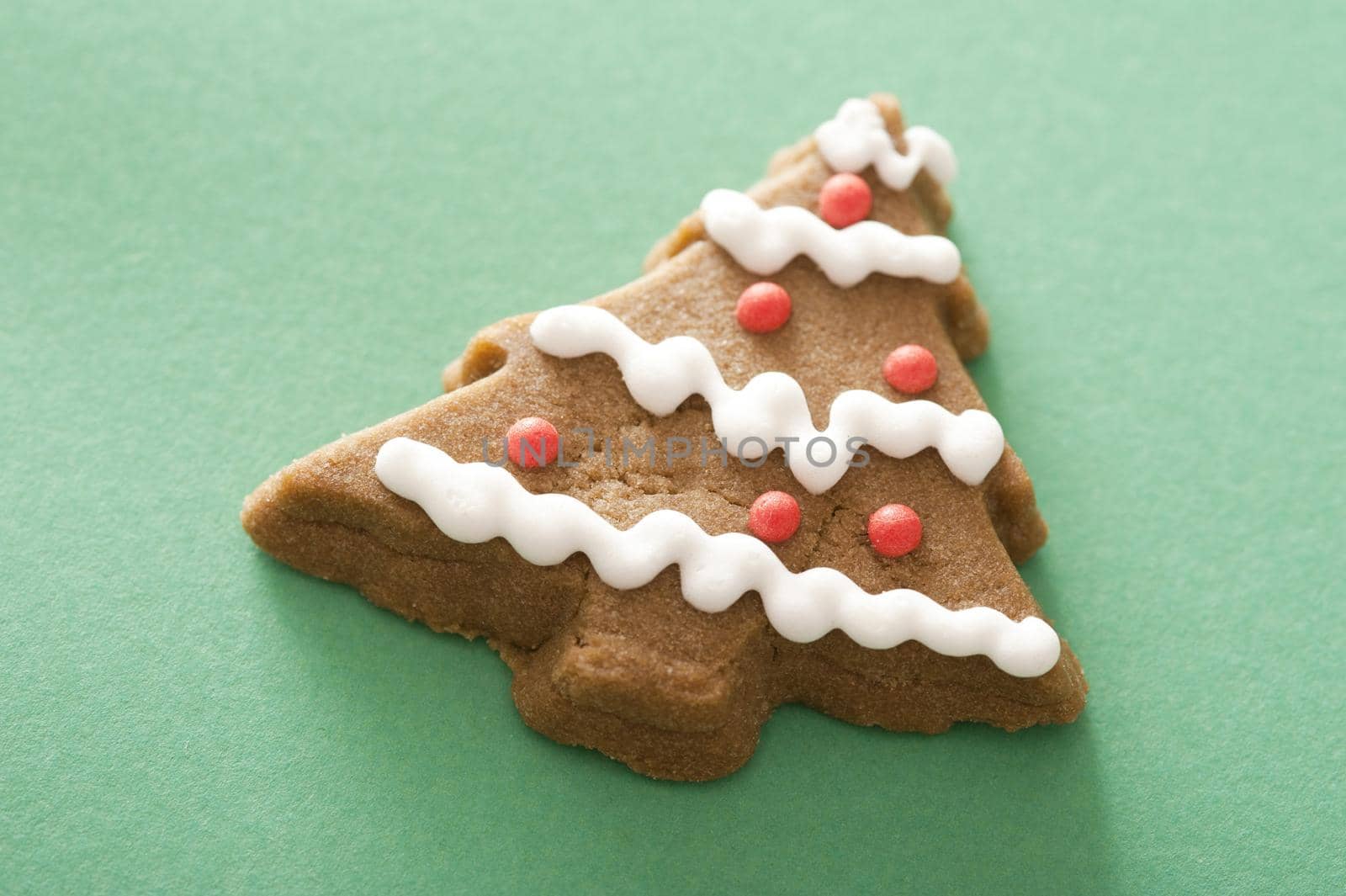 Christmas tree gingerbread cookie decorated with red and white icing on a green background with copy space