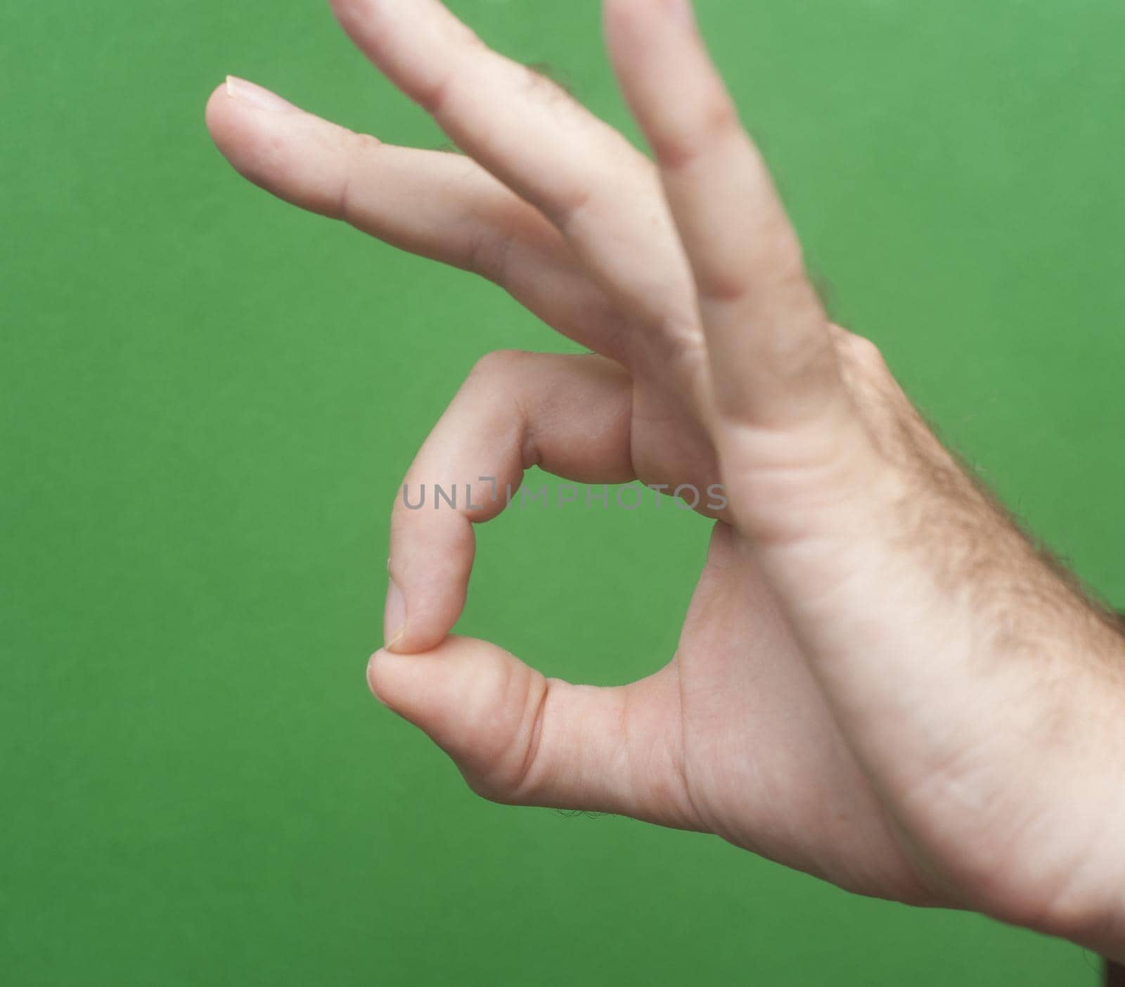 Man making a perfect gesture with his fingers over a green background to signal his complete satisfaction with a quality service or product