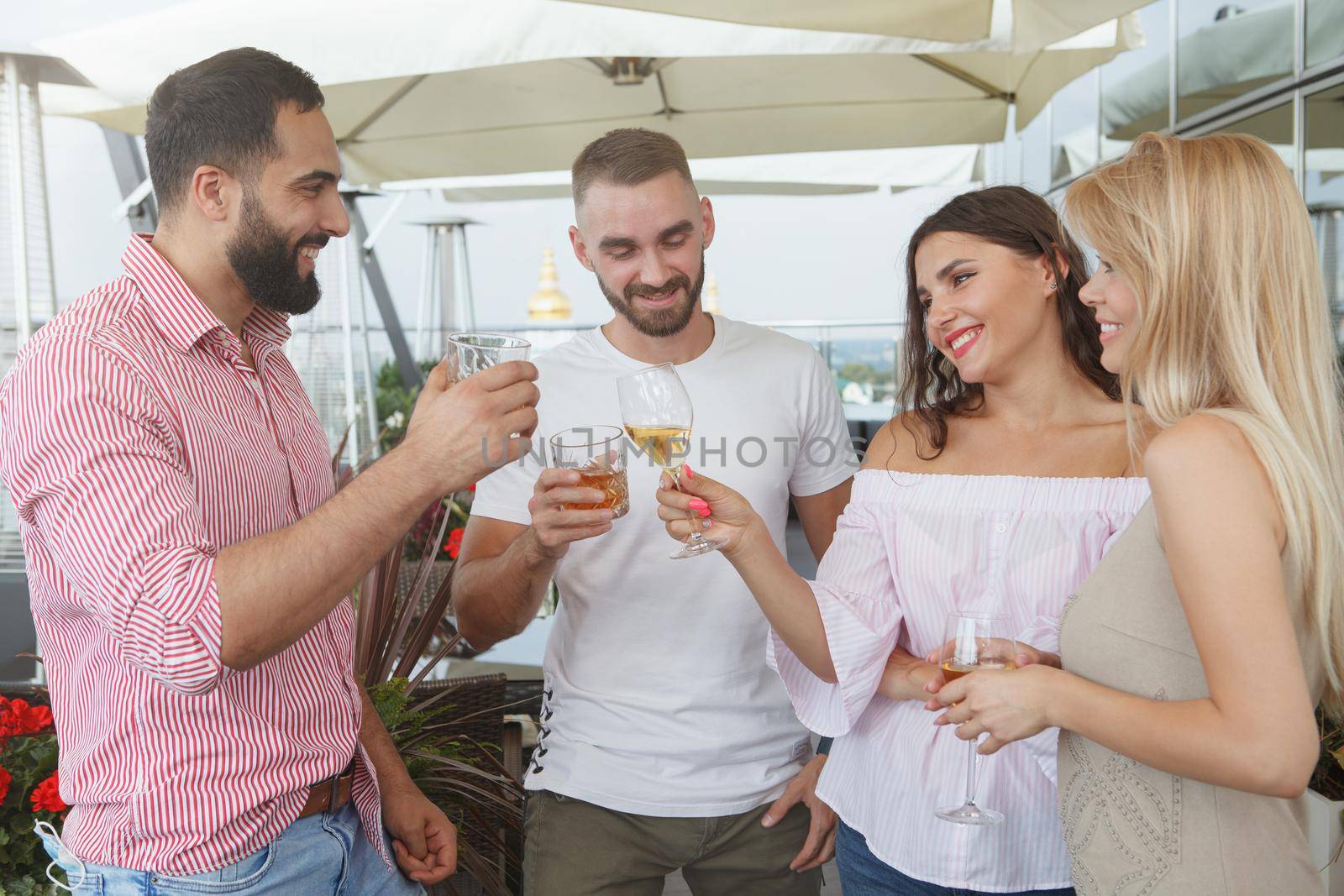 Group of friends chatting joyfully, having drinks at rooftop bar