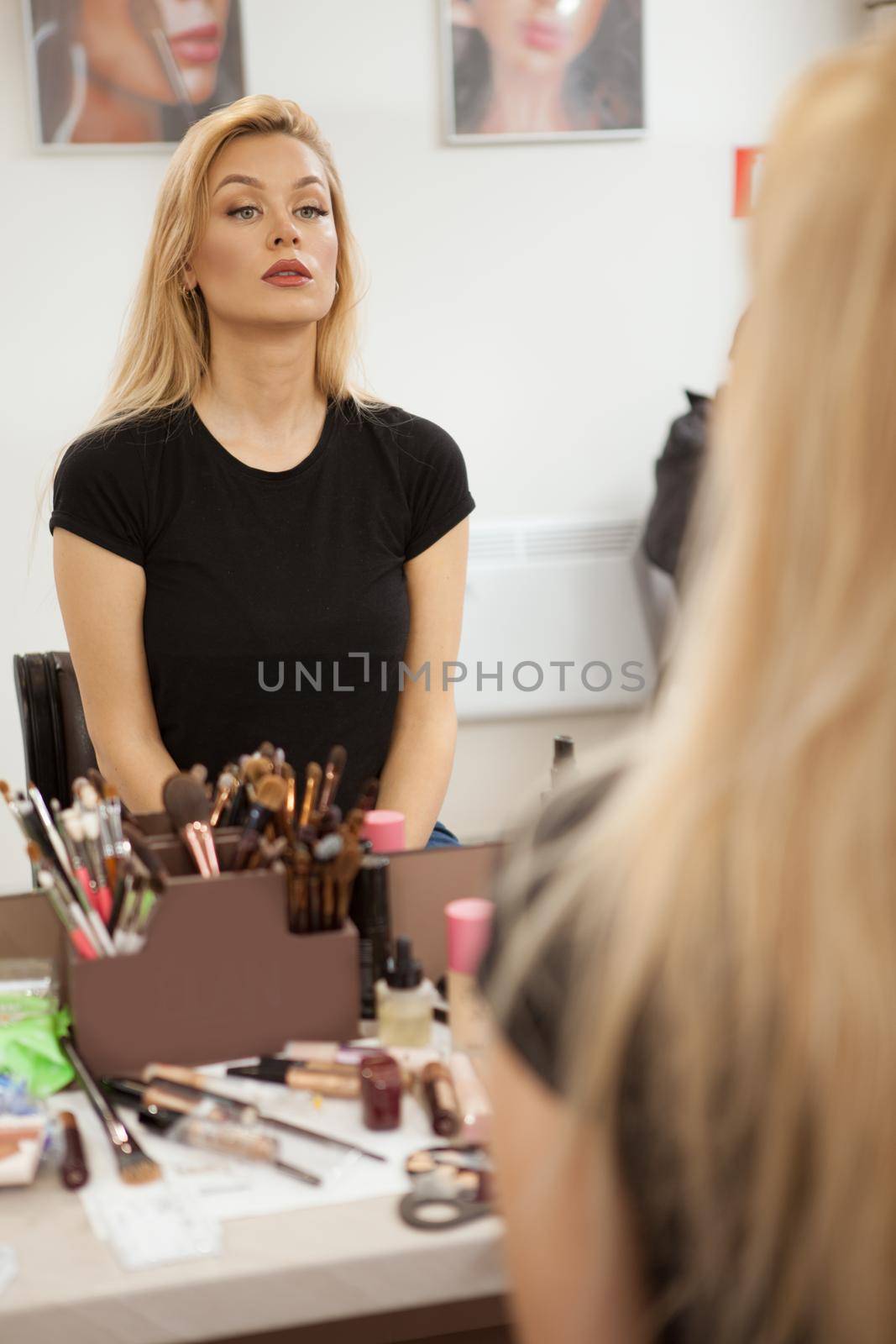 Vertical shot of a beautiful woman sitting in front of the mirror at makeup studio