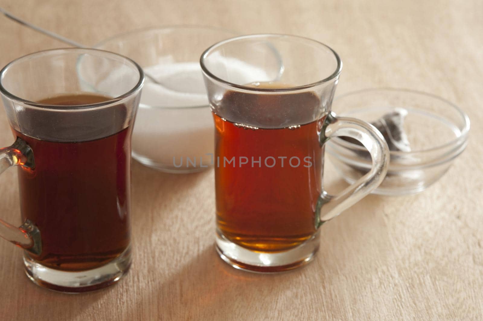 Two glass mugs of freshly brewed hot black tea with a bowl of sugar and the used teabags behind, high angle view