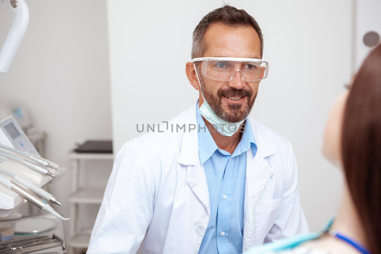 Cheerful mature male dentist smiling while talking to his female patient after dental checkup