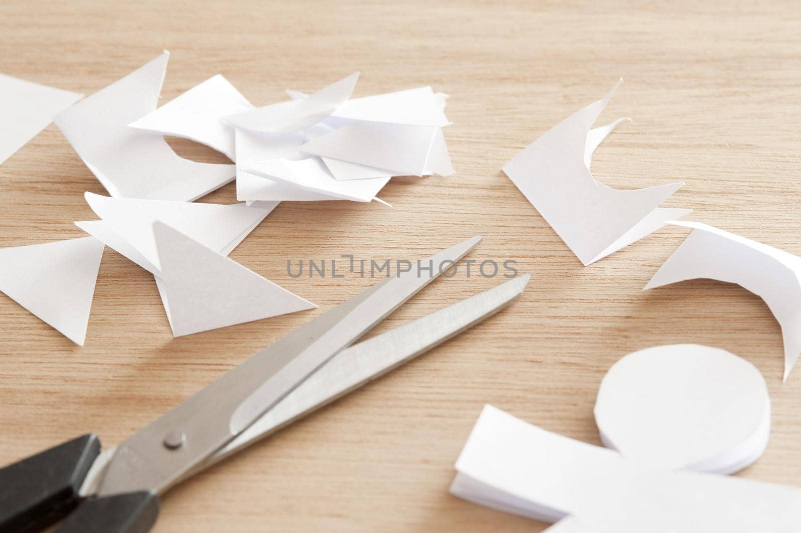 Paper craft concept with a pair of scissors and cut out of a doll or figure lying on a wooden table